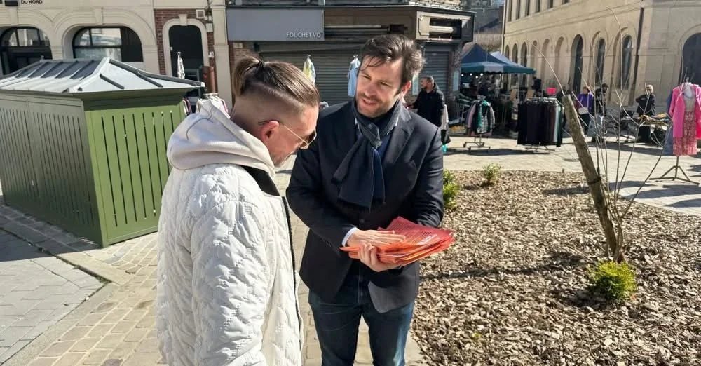 Un homme en costume noir et une cravate bleue échange des documents avec une autre personne portant un manteau blanc dans une zone urbaine, avec des étals de marché et des bâtiments en arrière-plan.