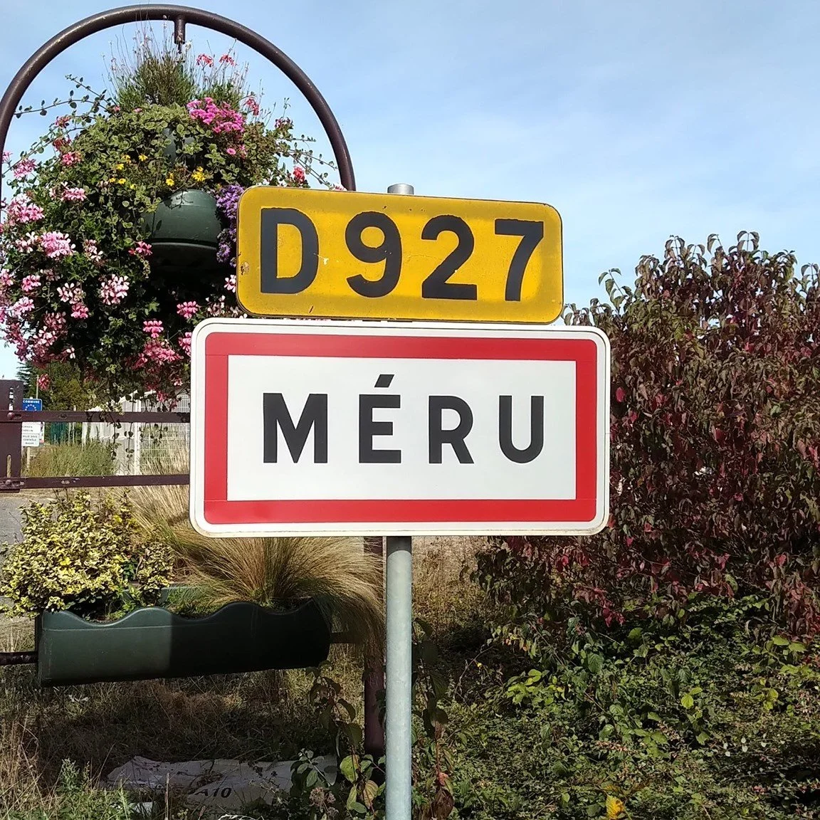 Panneau de signalisation indiquant la ville de Méru, avec un panneau jaune D927 et un panneau blanc avec le nom de la ville.