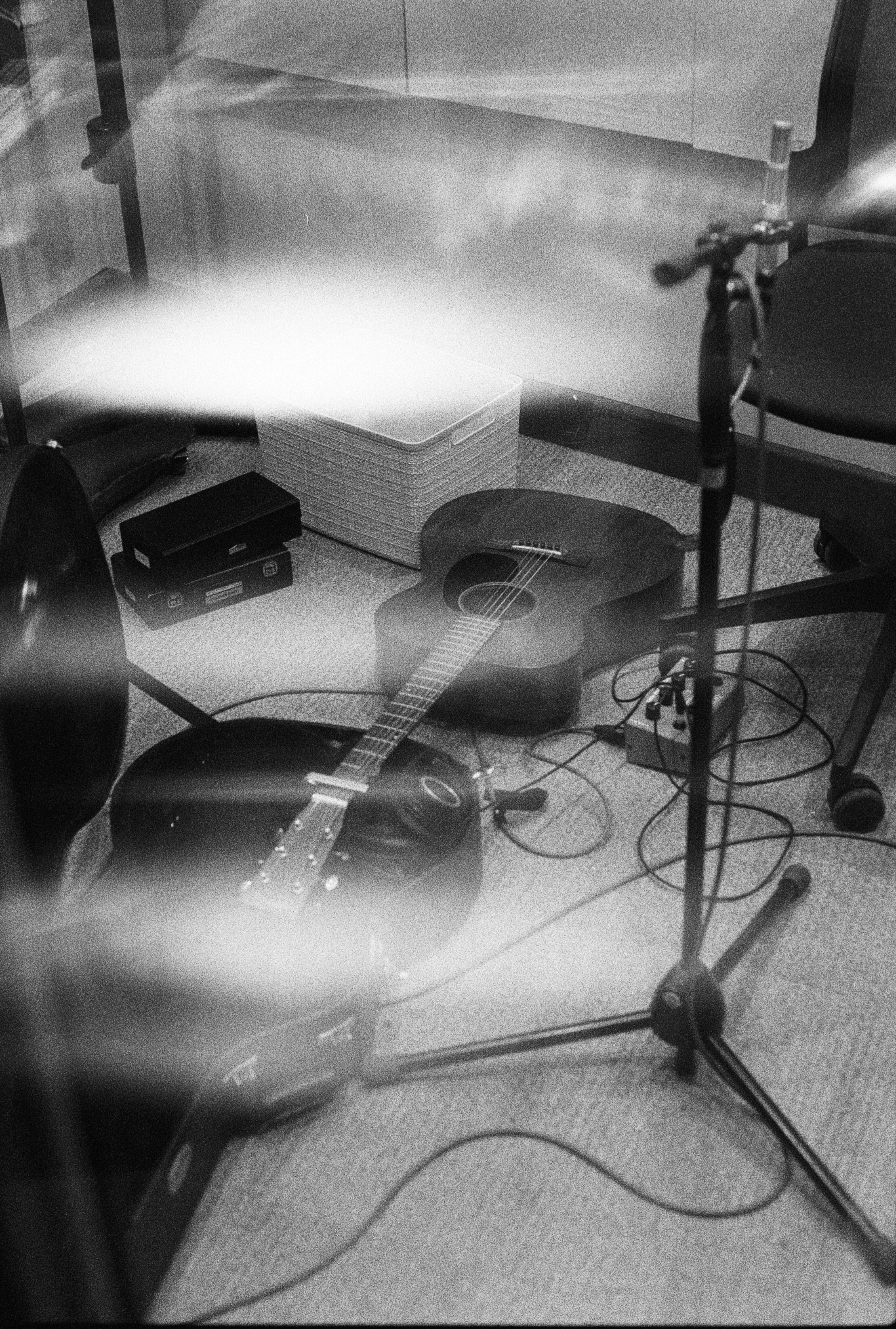 A guitar on a stand, music stand, microphone, speakers, and audio equipment in a room.