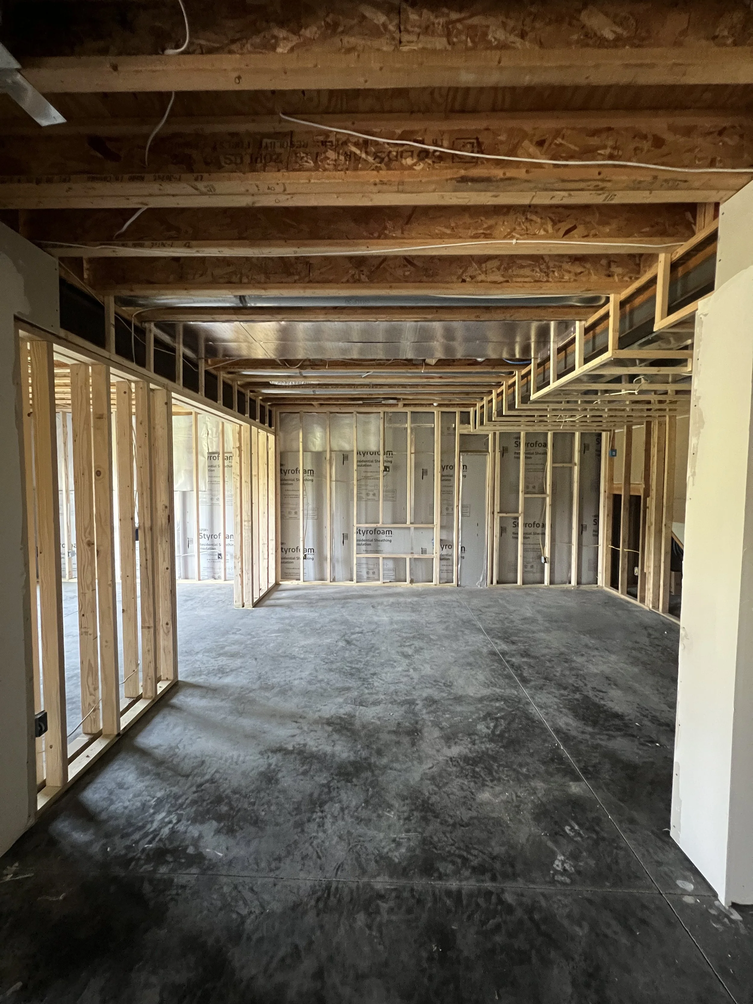 Interior of a house under construction showing exposed wooden framing, insulation, and unfinished concrete floor.