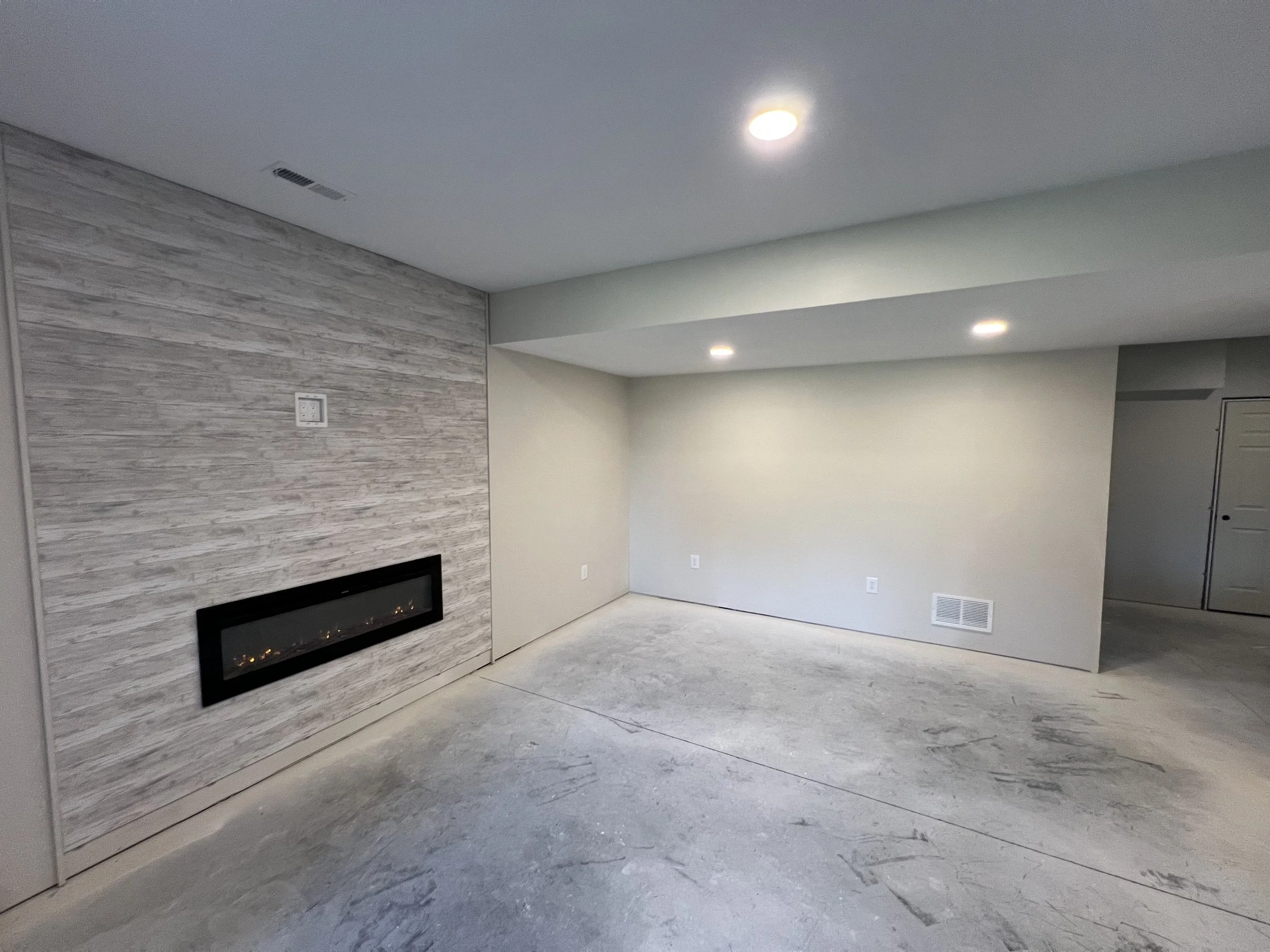Empty living room with a modern electric fireplace on a textured wall, and recessed ceiling lights.