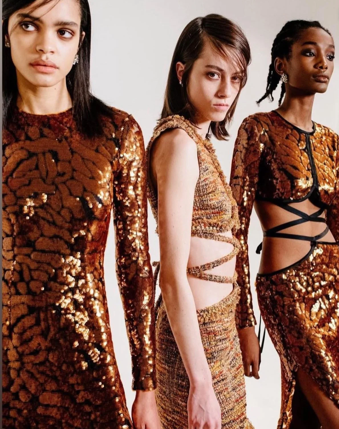 Three women in sequined orange and brown outfits standing side by side