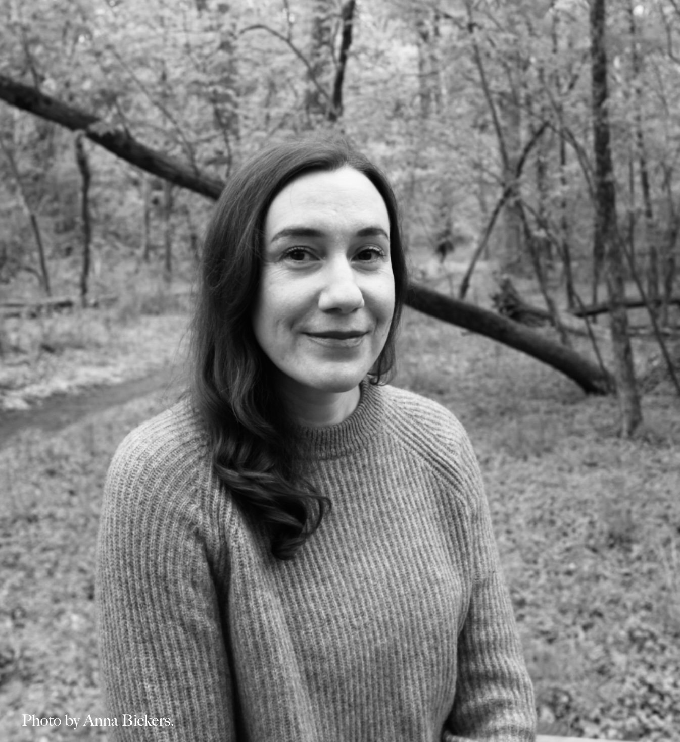 Catherine Champion with long wavy hair wearing a sweater outdoors in a wooded area, black and white photo.