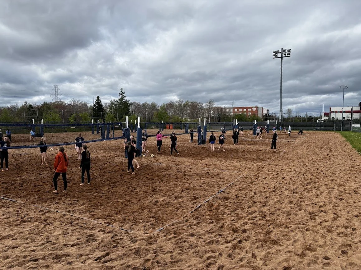 People practicing volleyball on an outdoor sandy court with overcast skies.