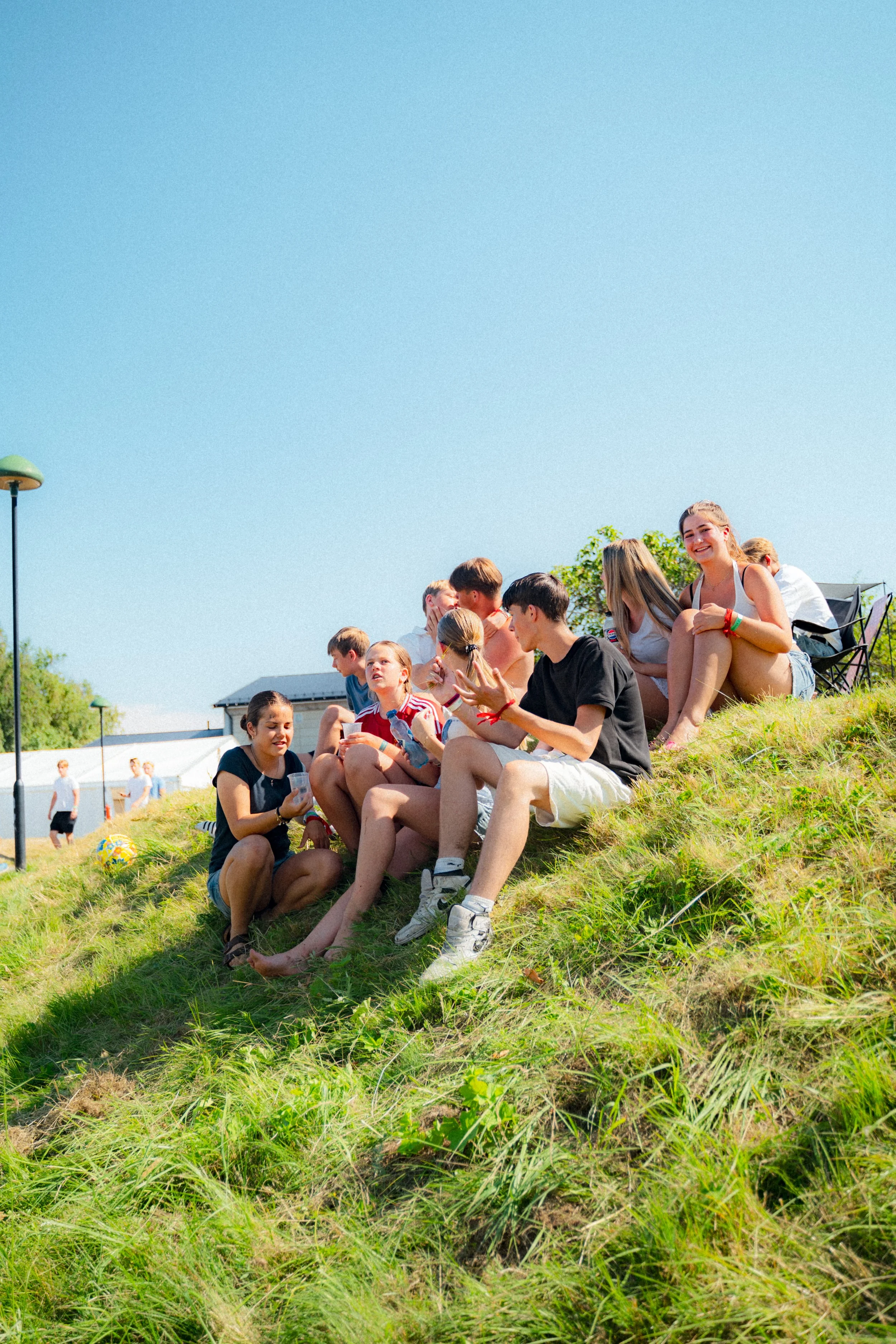 En gruppe deltakere sitter og prater på en grønn ås under en klar blå himmel.