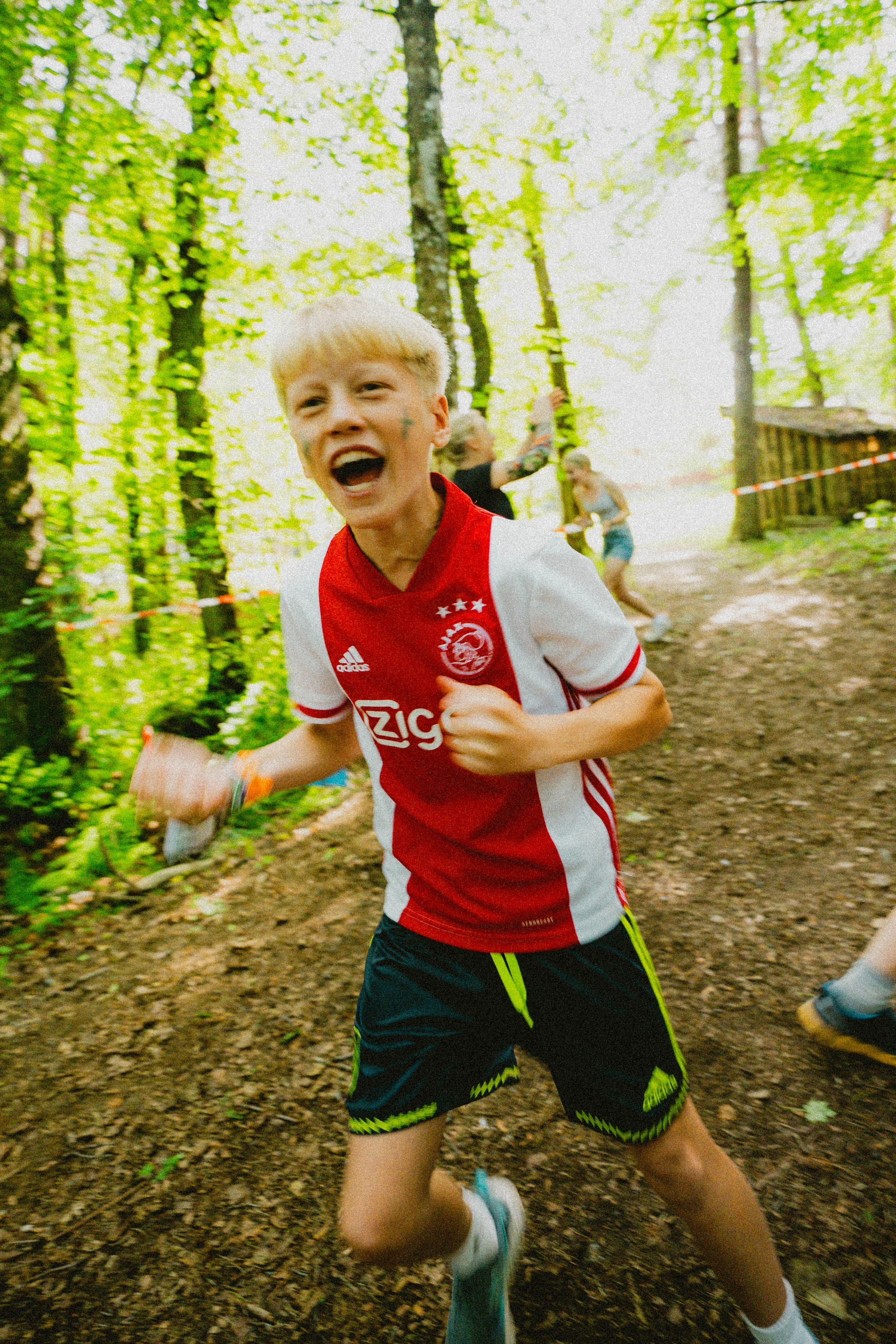 En ung gutt løper og ler i en skog under en Capture the Flag.