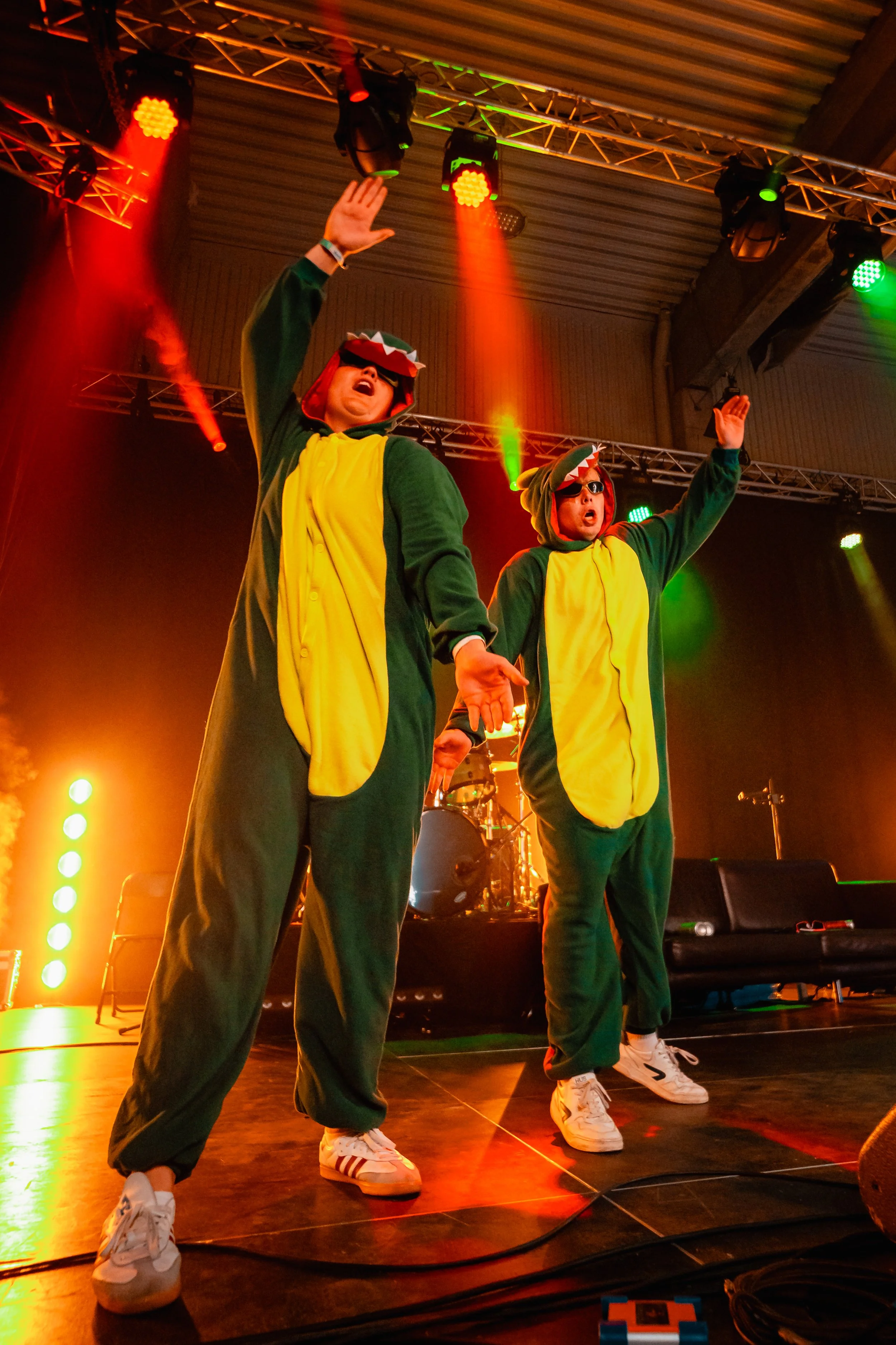 To personer i dinosaurkostymer som opptrer på en scene med fargerike lys.