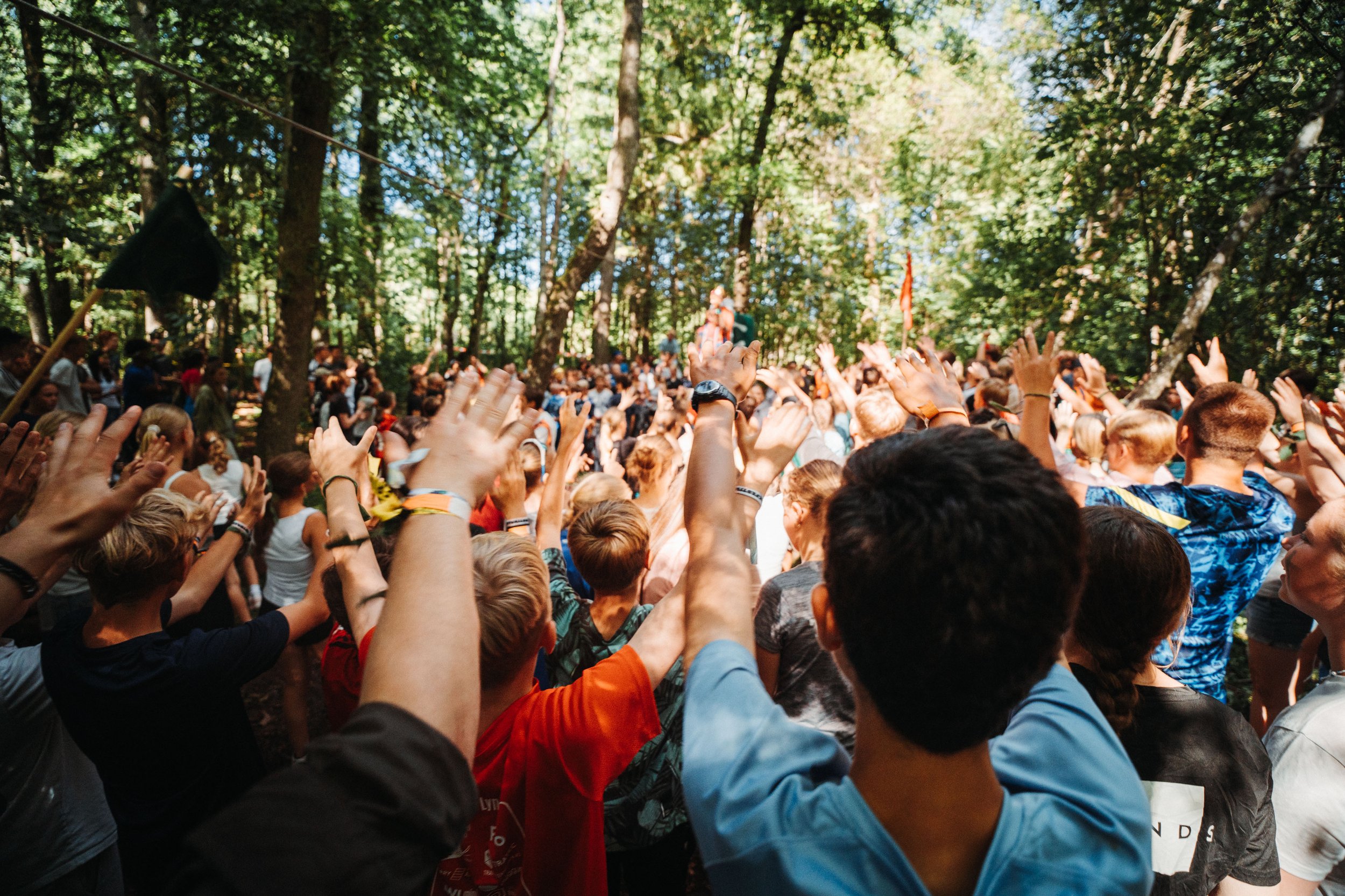 En stor gruppe deltakere som samles i en skog, med hender hevet i luften. Alle er giret for en runde med capture the flag.