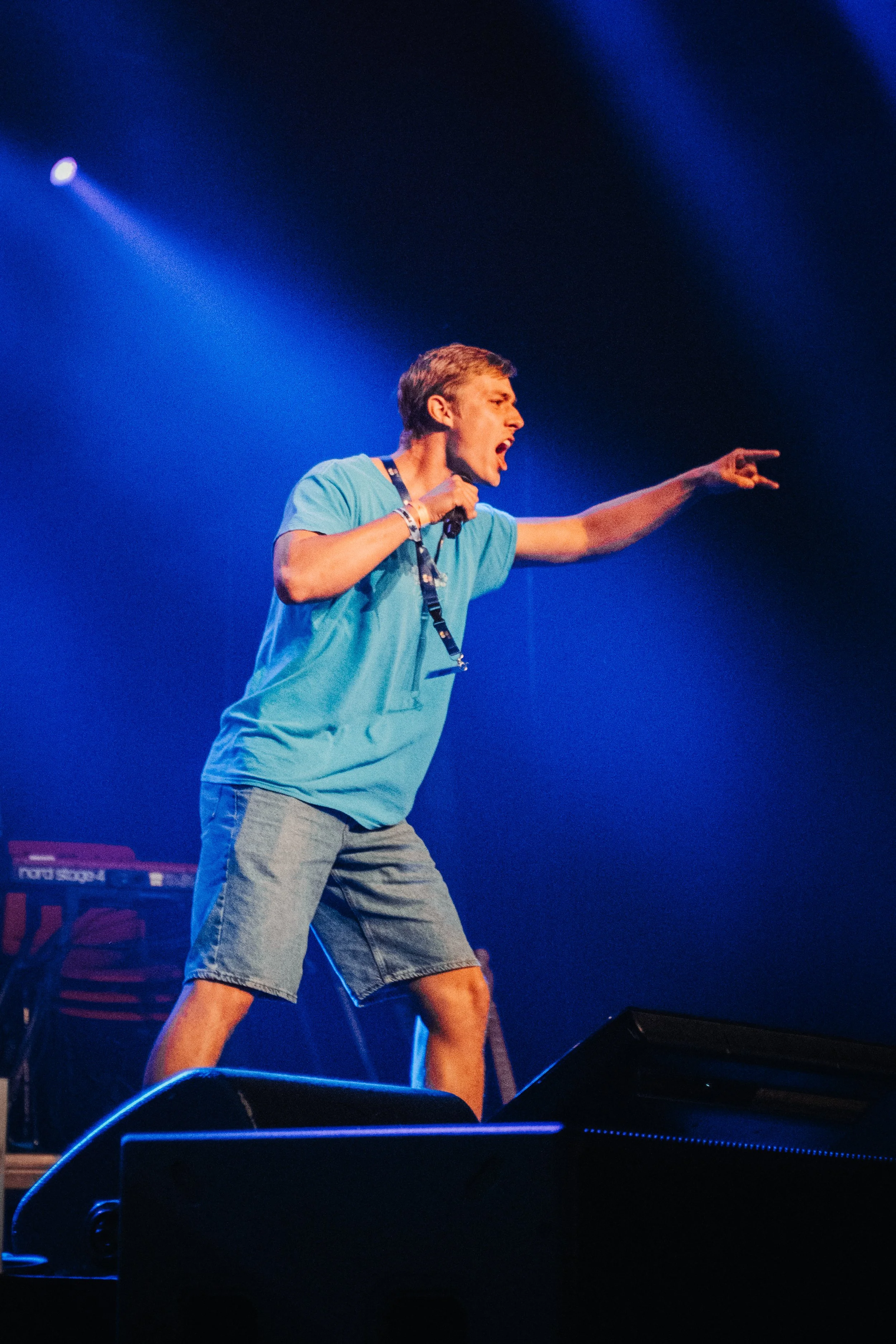 En mann på scenen som roper eller synger med en hånd utstrakt, bakgrunnslys i blått.