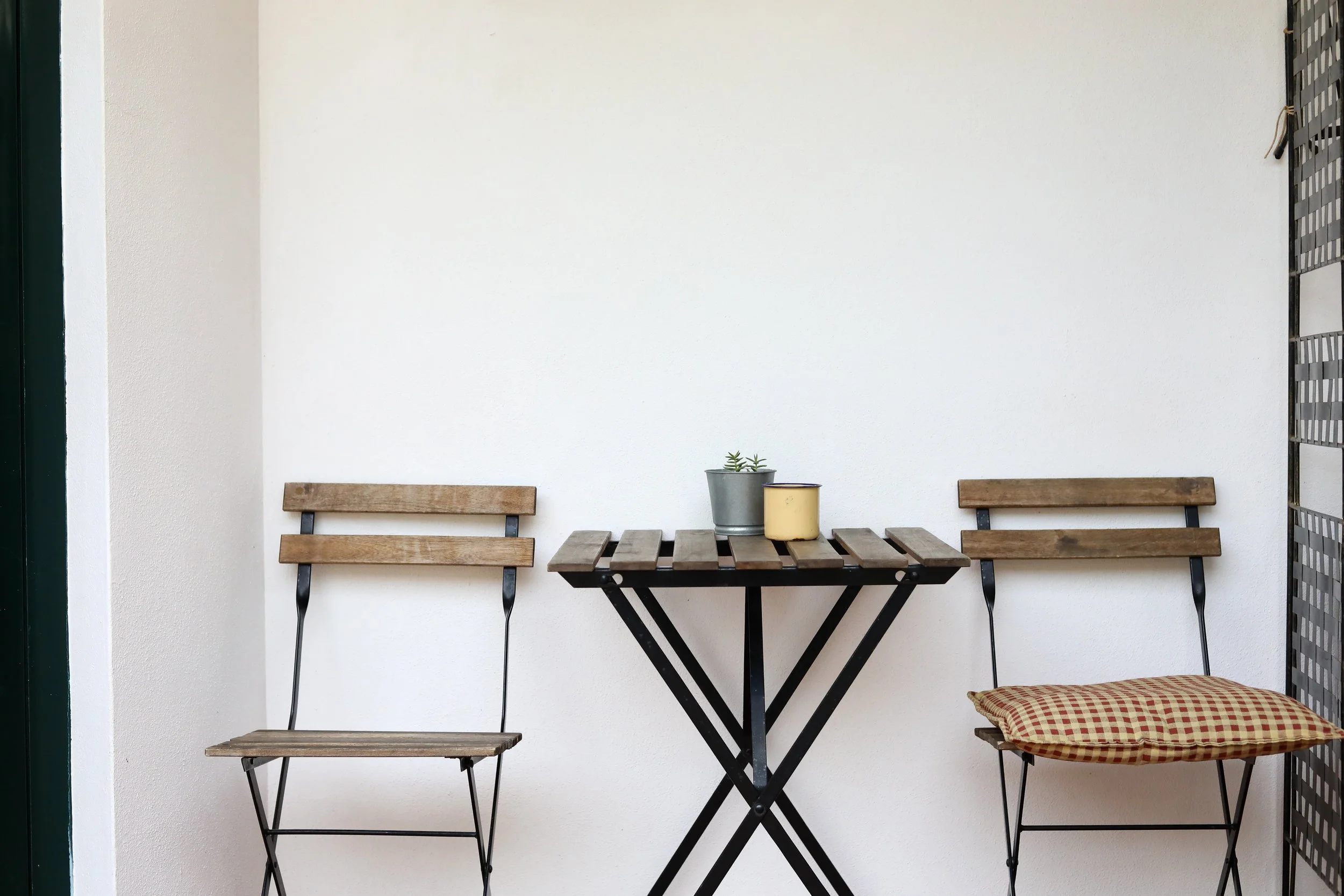 Mesa com duas cadeiras de ferro e madeira, uma com almofada de gato, na varanda