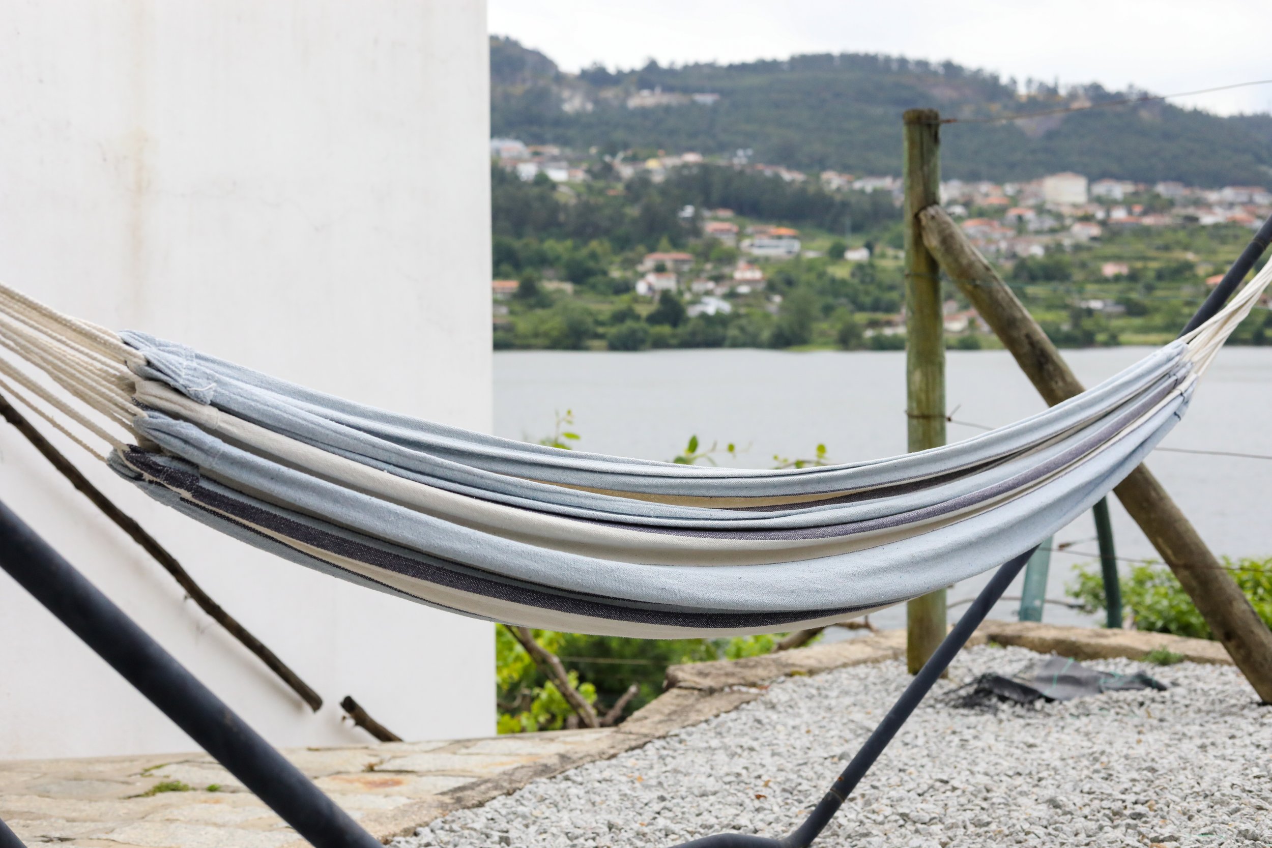 Rede de descanso em um espaço externo com vista para um rio e uma área residencial em uma colina ao fundo.