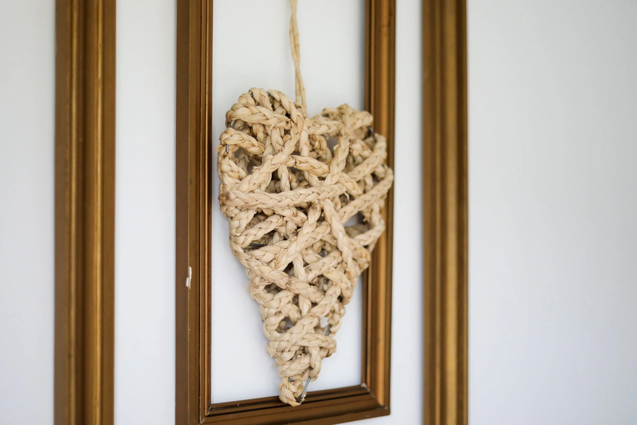Decorativo painel com coração feito de corda natural, em moldura dourada na parede.