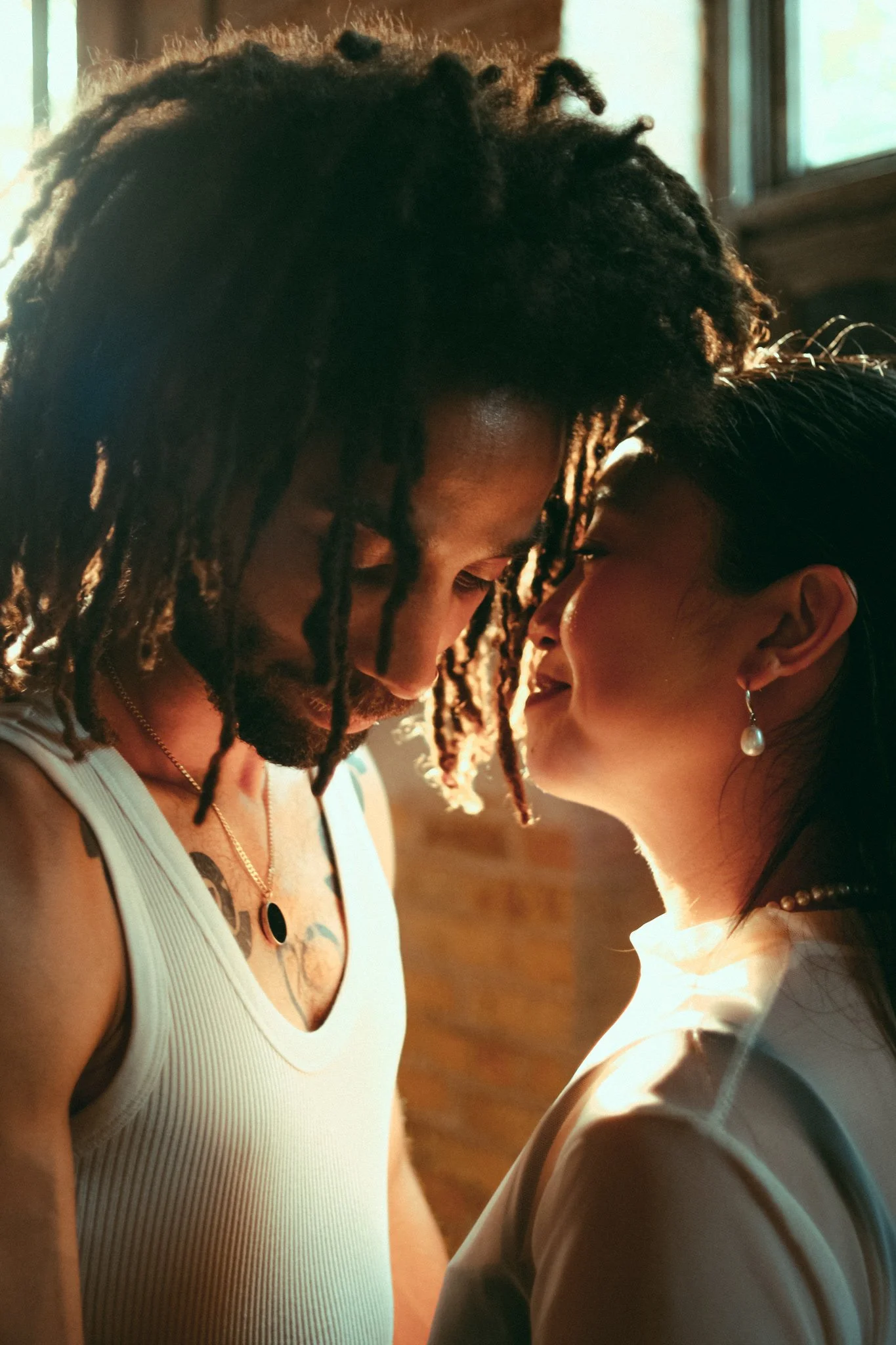 A close-up of a black man and an Asian woman touching foreheads in an intimate moment with soft lighting.