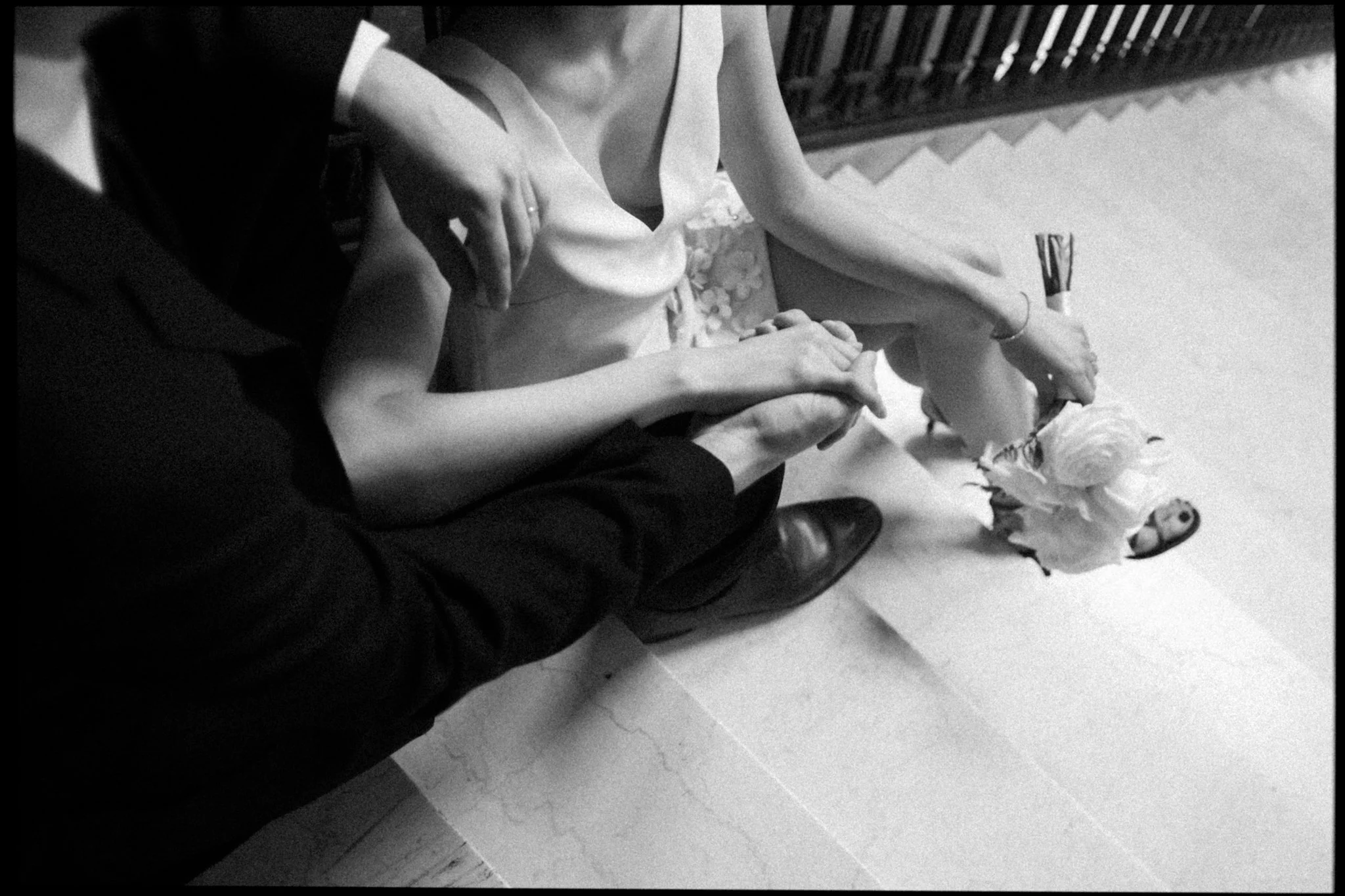 Black and white photo of a couple sitting on the ground, holding hands, with flowers nearby, outdoors at night.