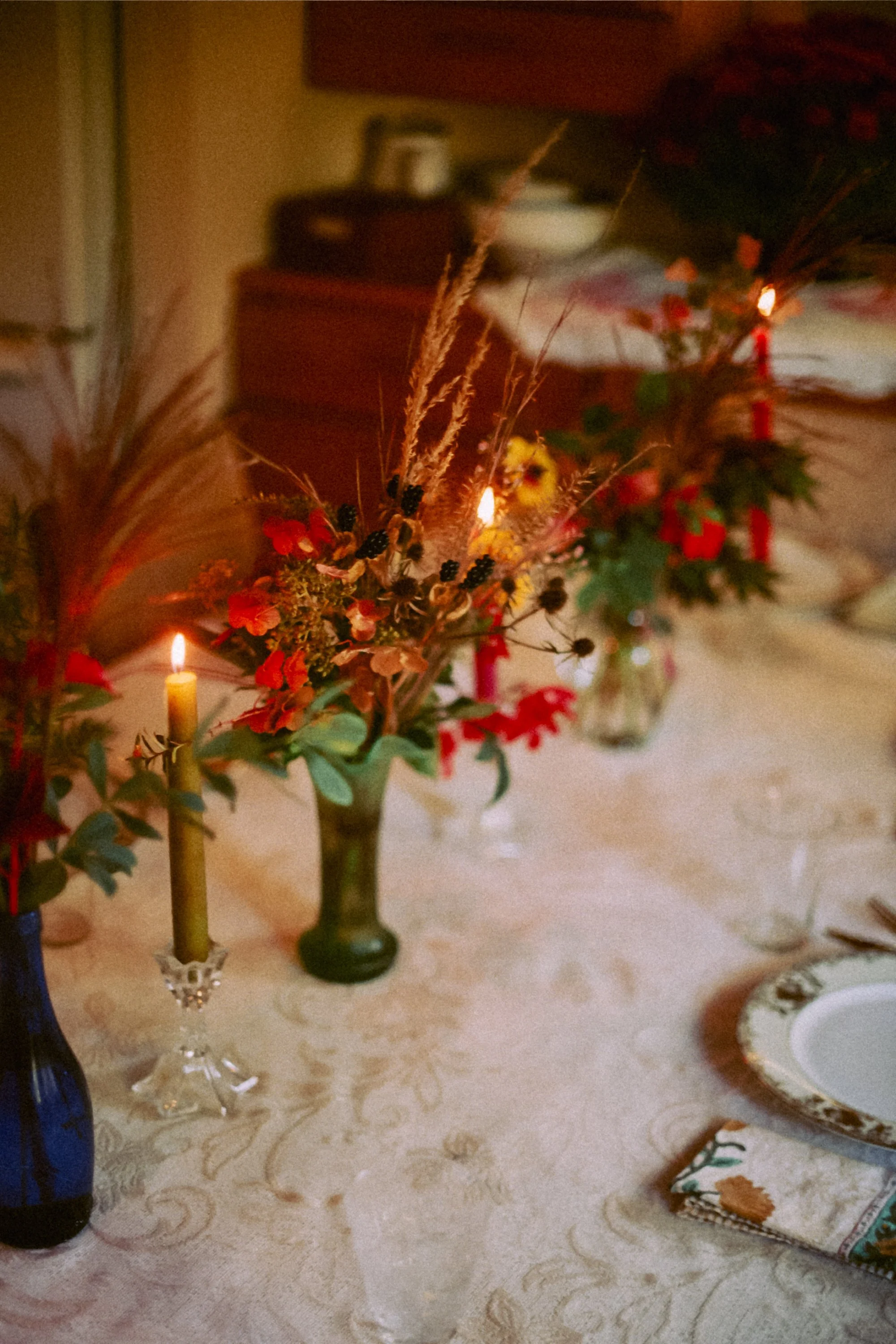 A table decorated with a fall floral centerpiece, lit candles, and holiday-themed dishes and napkins.