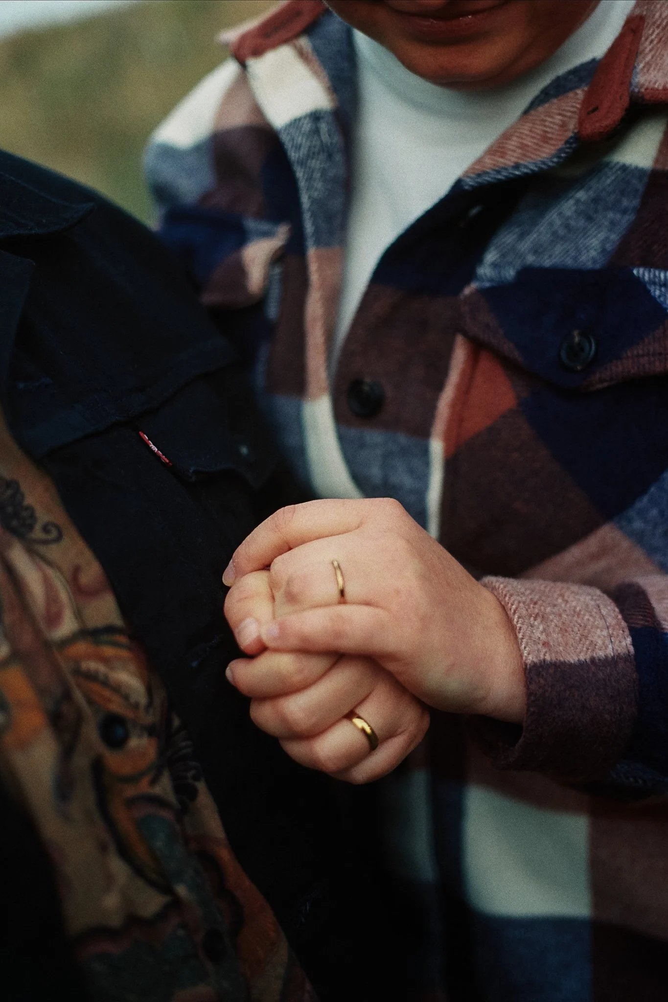 A person wearing a plaid shirt and rings on their fingers is holding the arm of another person wearing a black jacket.