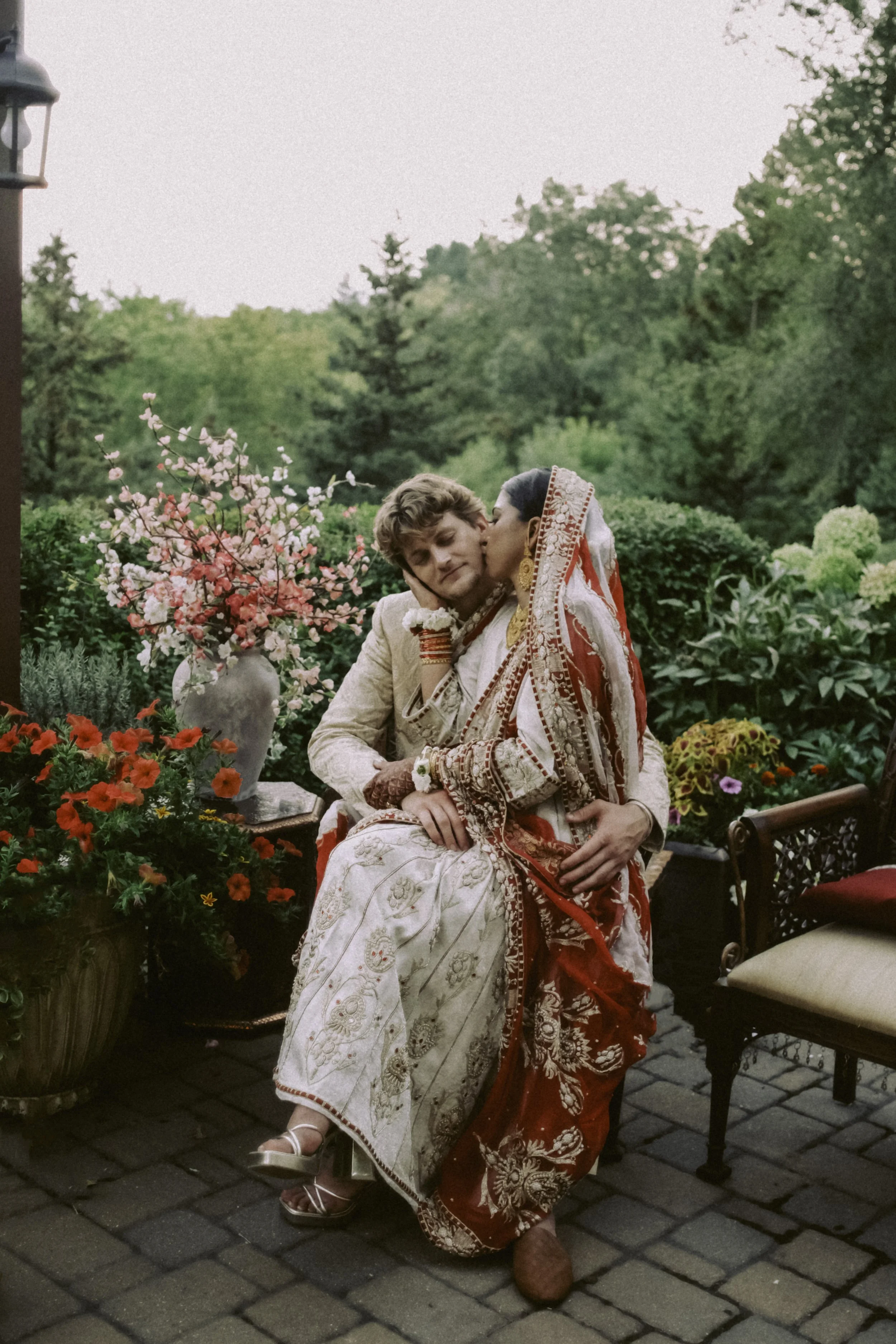 A man and woman in wedding attire sharing an intimate moment outdoors on a patio with flowers and greenery in the background.