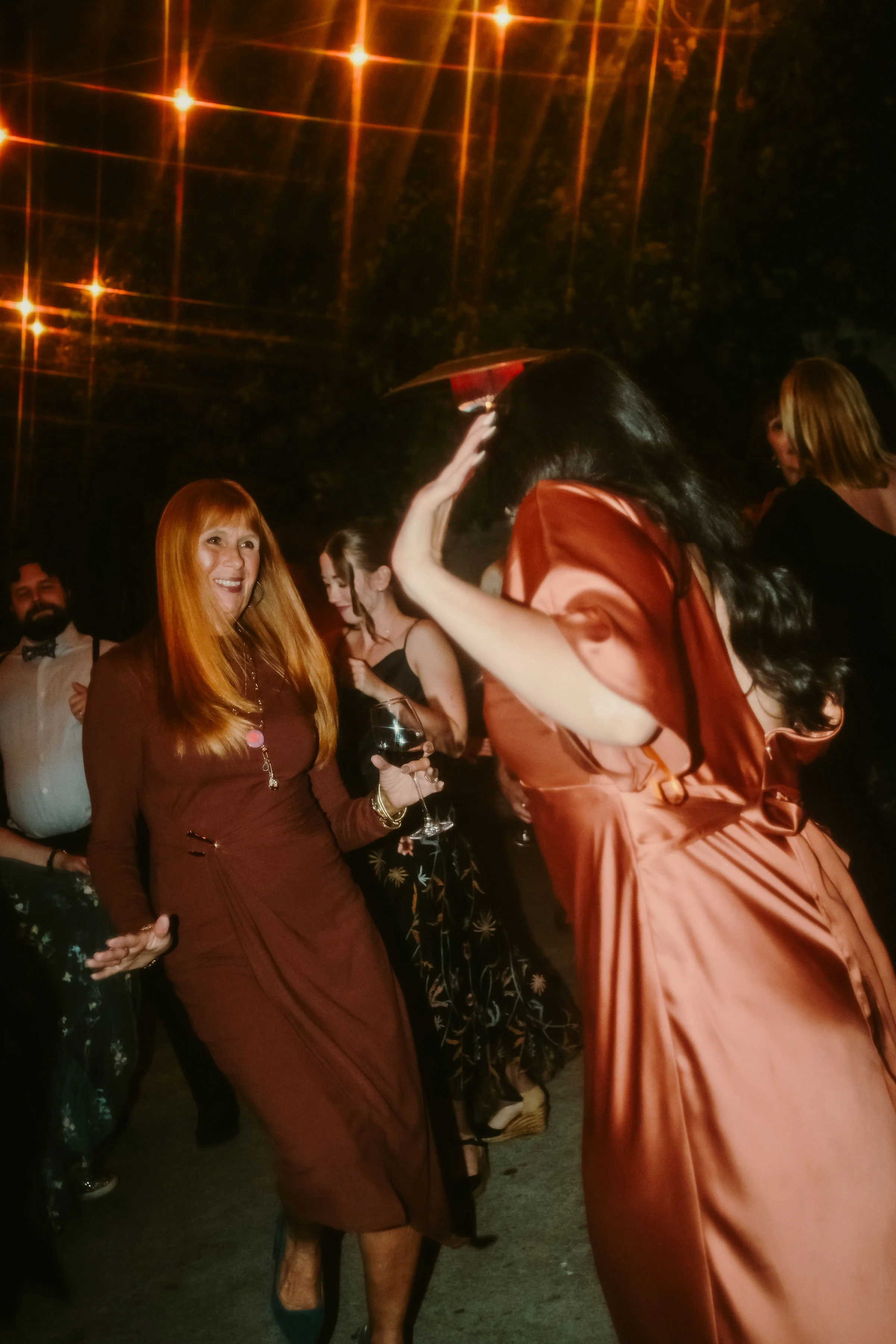 People dancing and socializing at an outdoor nighttime party with string lights overhead.