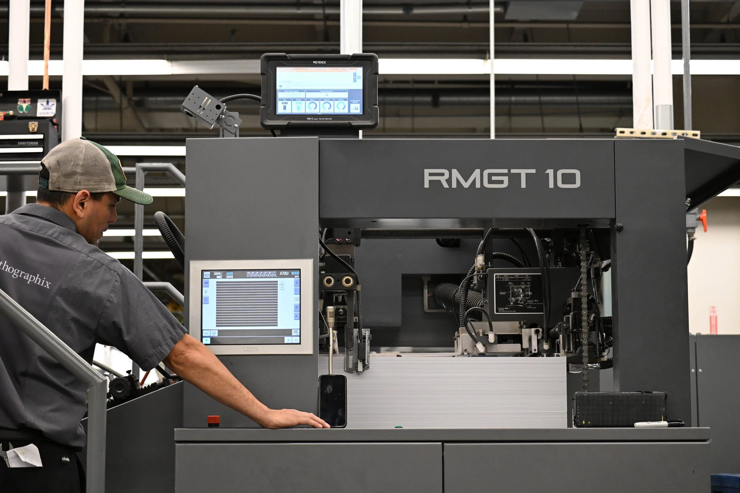 A worker operating a large industrial machine labeled 'RMGT 10' in a factory setting, with control screens and machinery.