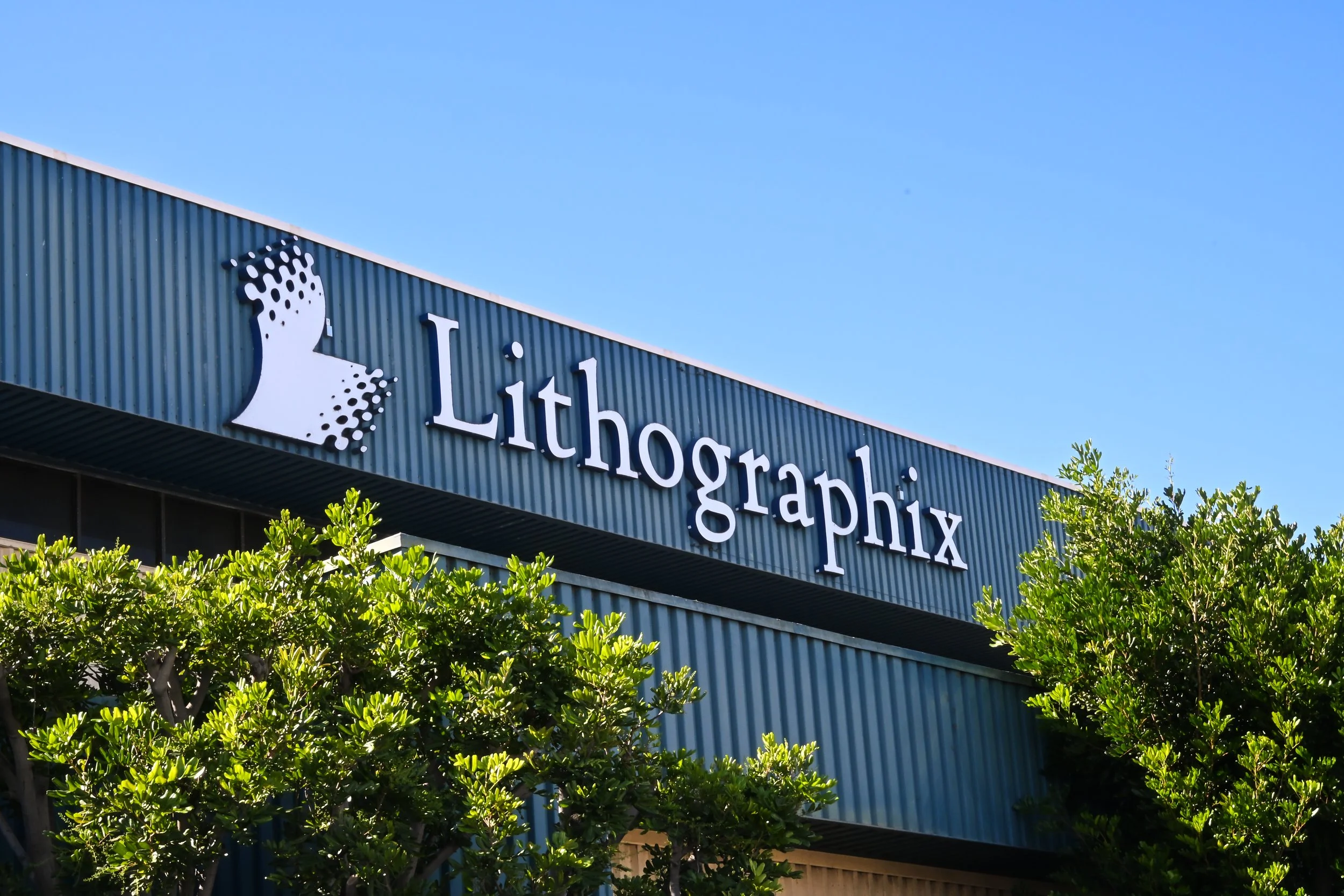 Signboard for Lithographix with a logo and trees in the foreground.