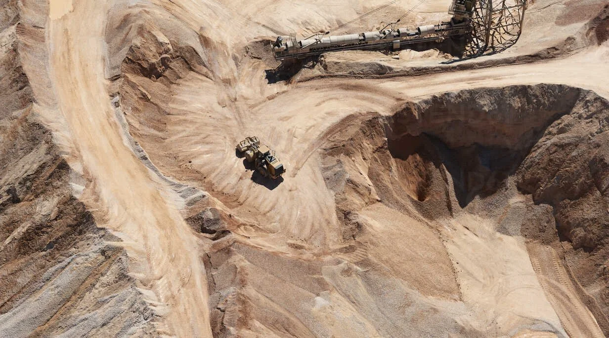 An open-pit mining operation with trucks and machinery working in a large quarry of sand and rocks.