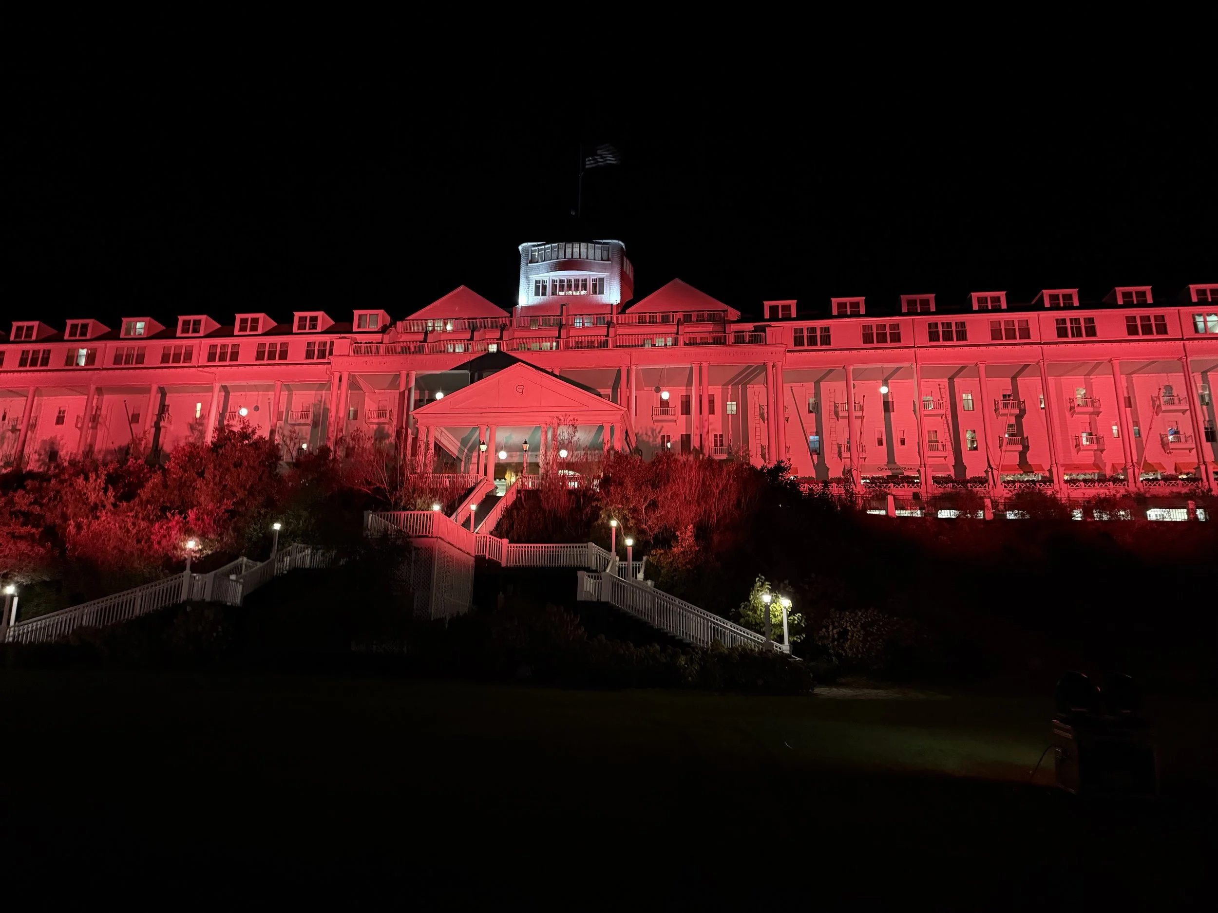 Grand Hotel on Mackinac building illuminated in red orange lights at night, with a dark sky and some trees in the foreground. Changeable to any occasion or lighting. Halloween Celebration weekend 2025.