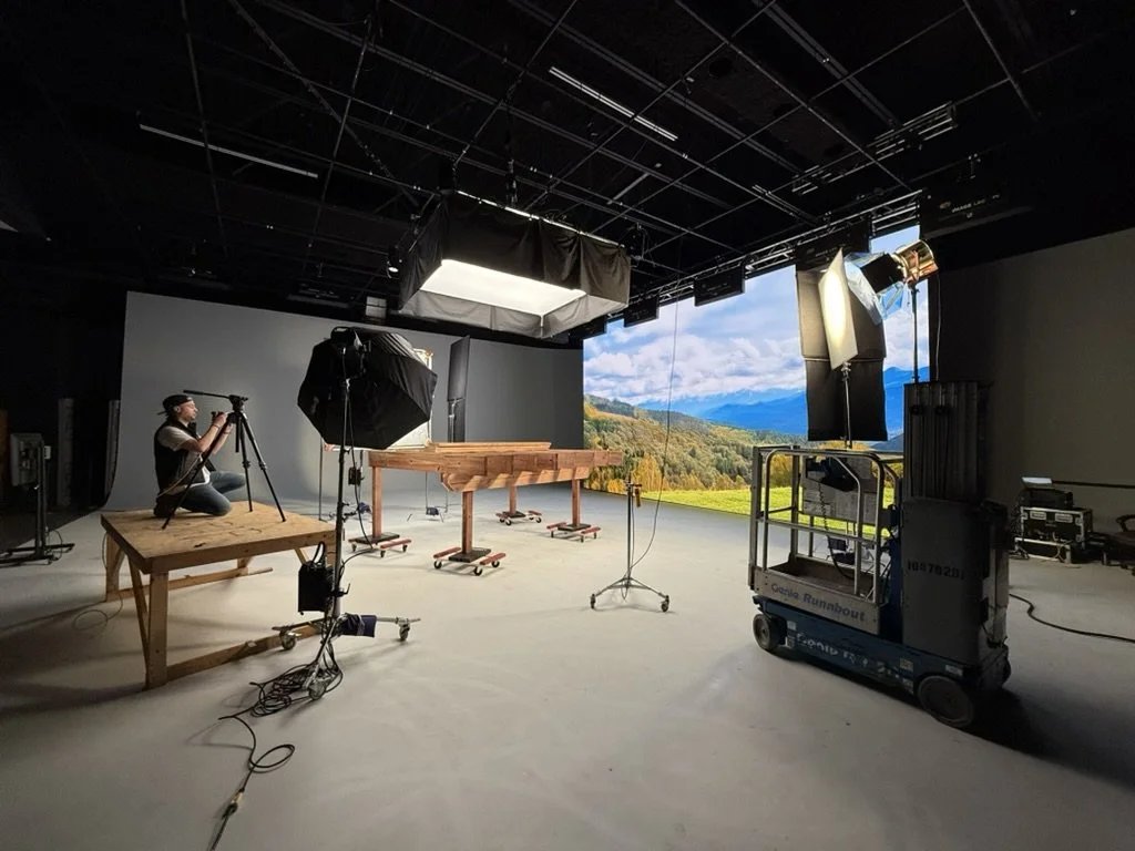 A professional video or photo studio with lighting equipment and a large video wall LED screen backdrop showing a scenic landscape of mountains and blue sky. Used for advertisements and promotional content.