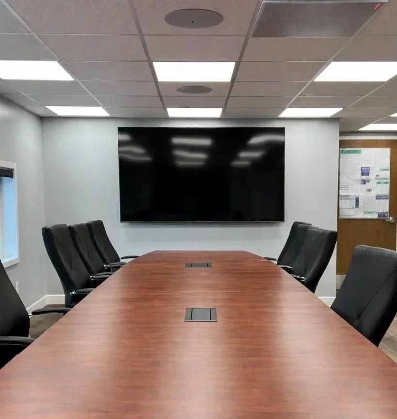 Utility Contracting post installation conference room with a conference table, black leather chairs, a large black monitor on the wall, and out of sight microphones and speakers in the ceiling providing crisp audio.