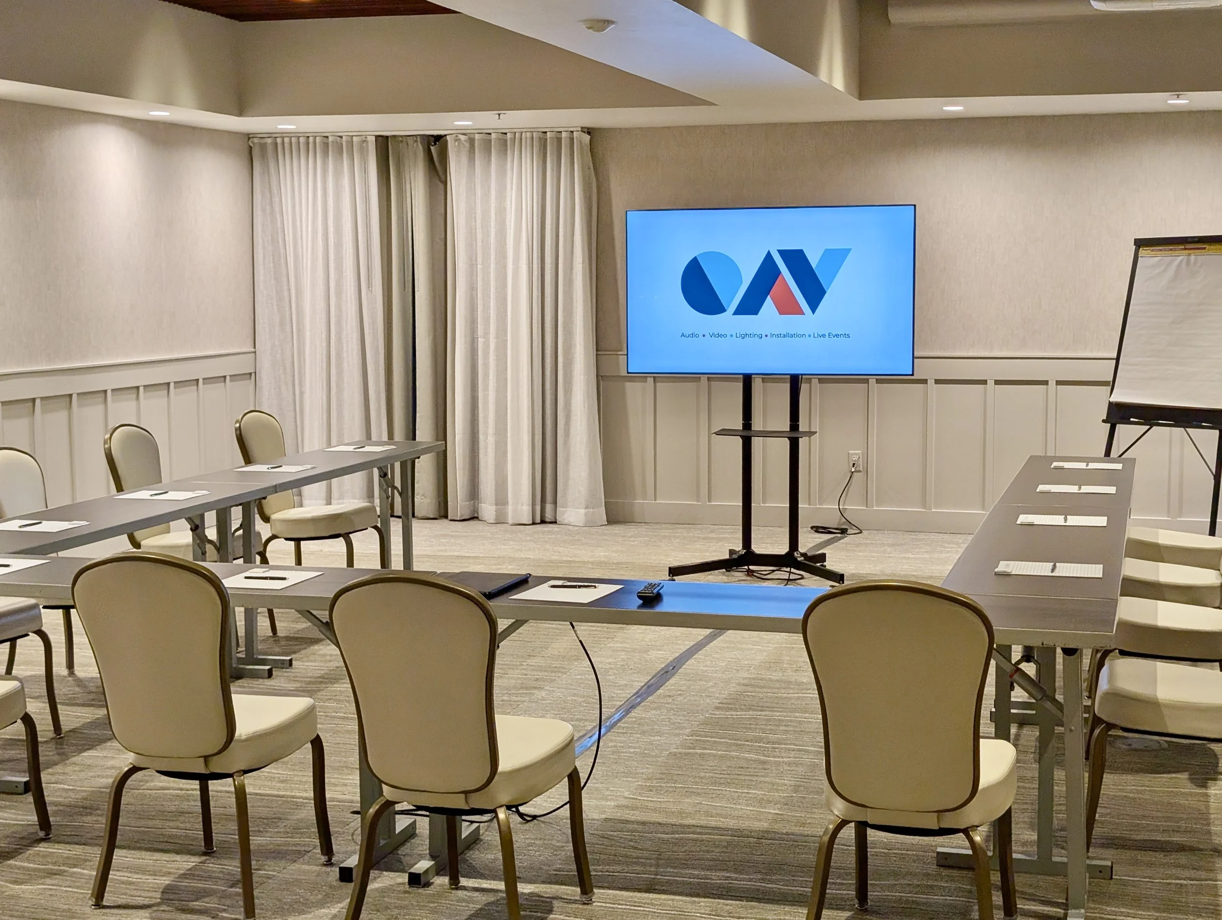 A U-shape conference room setup, portable large screen displaying a meeting content and audiovisual related services, and a flip chart with paper, ready for a presentation or meeting. At Delamar Hotel in Northern Michigan, managed av services.