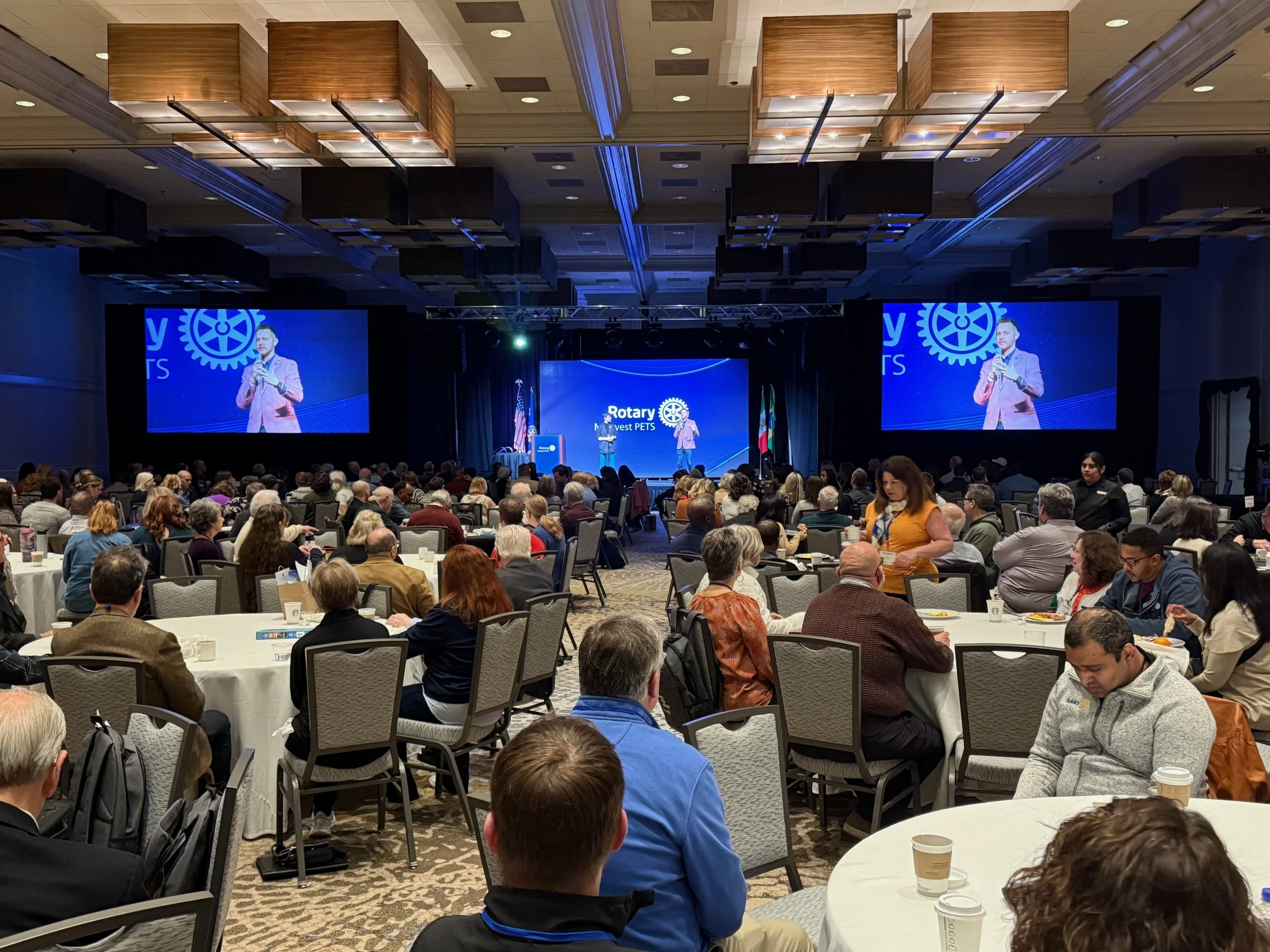 A large conference room audiovisual setup, video wall backdrop, stage, dual projection, full audio, video, lighting, and rigging, with a Speaker on stage at a Rotary event displaying a Rotary logo in Chicago, Illinois.