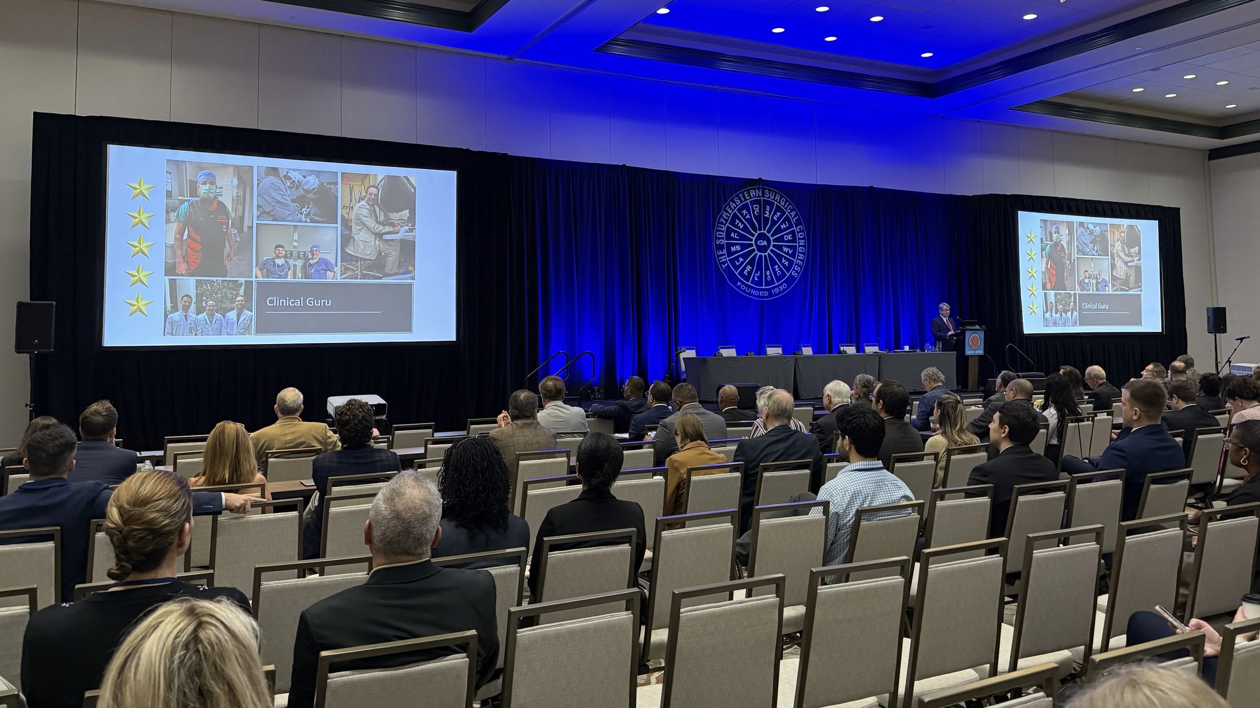 The Southeastern Surgical Congress 2026 conference, Fernandina Beach, Florida. General session with attendees seated in. Two large screens display slides. Blue lighting, pipe and drape and the conference logo projected with a gobo projector.