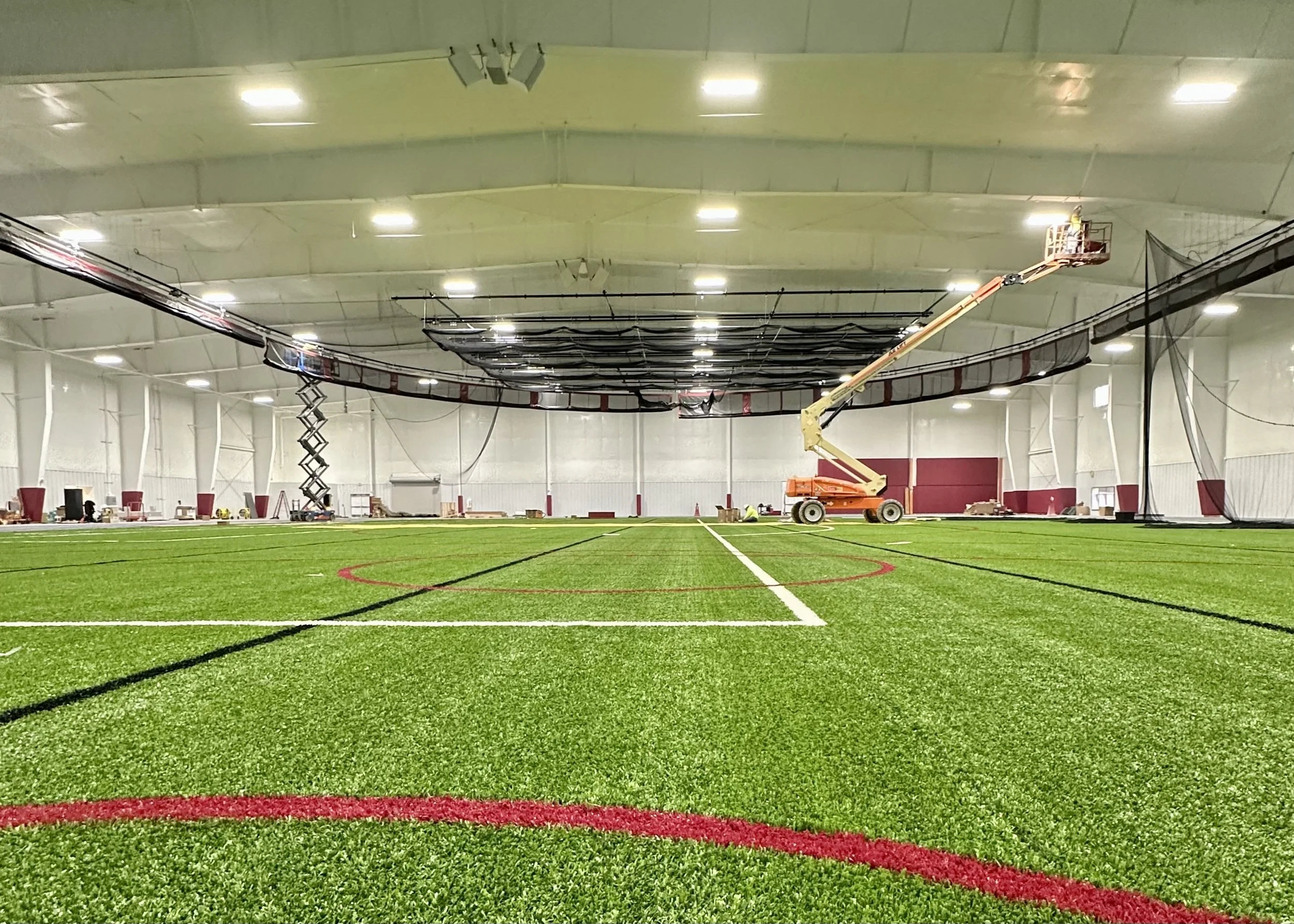 An indoor sports field at a college, a large crane and lift to install speakers and amplifiers to the ceiling for an audiovisual installation repair. Alma College Field House, av setup is compatible with all college indoor sports fields.