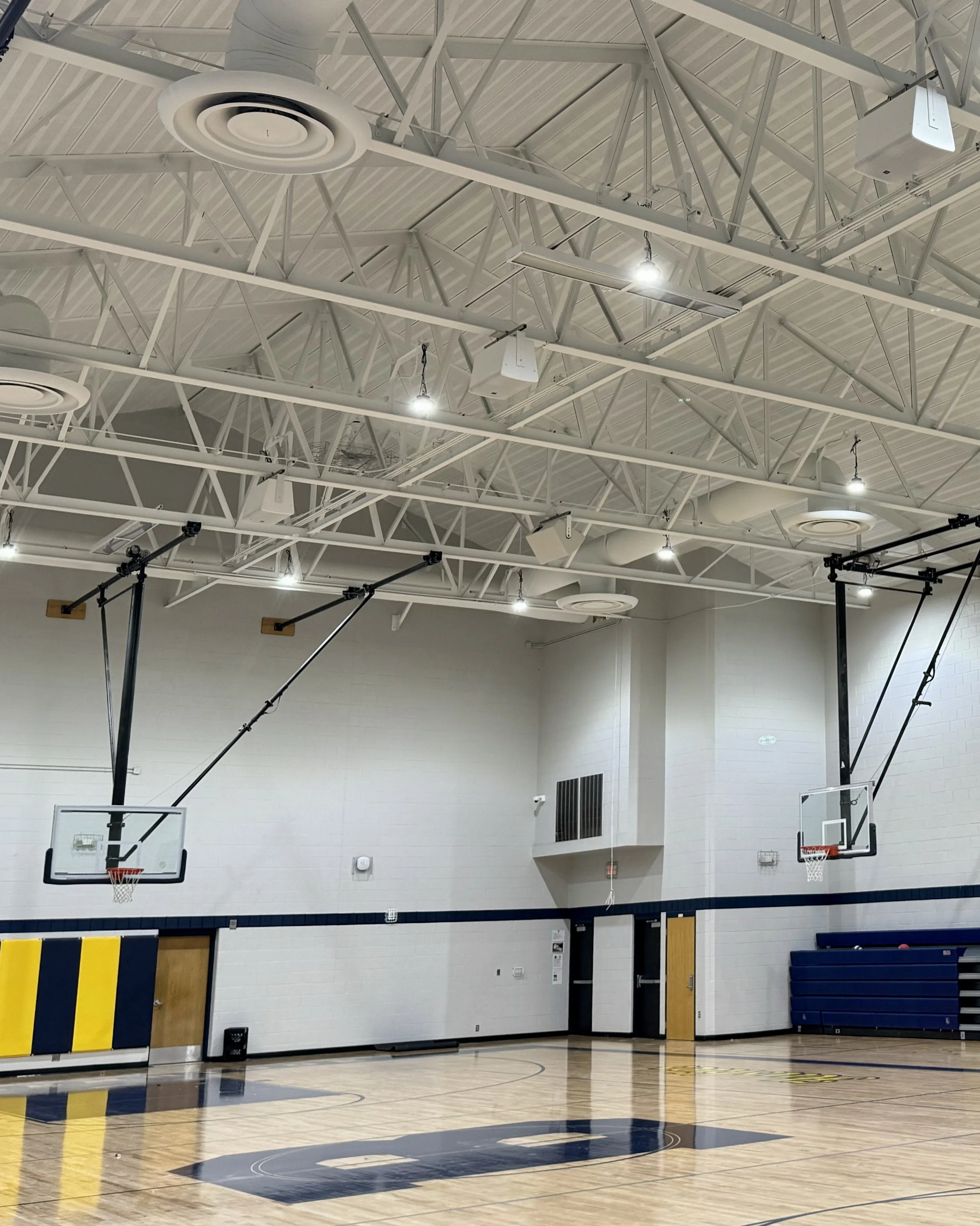 Breckenridge middle School indoor basketball court inside a middle school gymnasium with banners hanging on the walls and a scoreboard. Audiovisual installation of speaker and sounds, AV control console on the wall. Speakers blend in with ceiling.