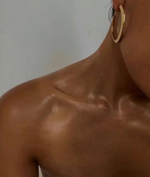 Close-up of a woman's shoulder, neck, and part of her face with a hoop earring, showing smooth, tan skin.