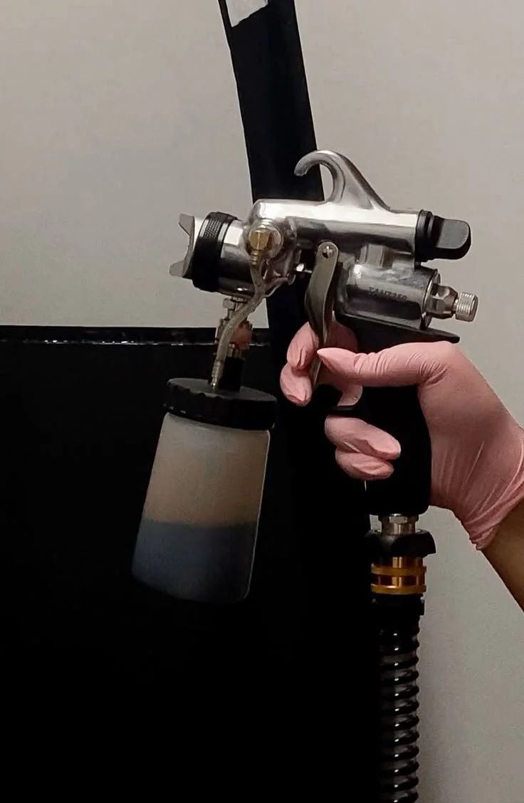 A person wearing pink gloves holding a tattoo gun with a black tube and a ink cup, ready for tattooing.