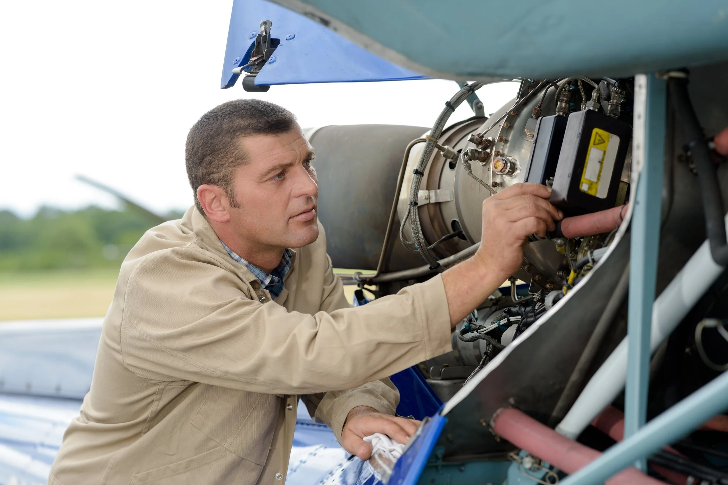 A man inspecting or repairing the internal components of an aircraft engine outdoors.