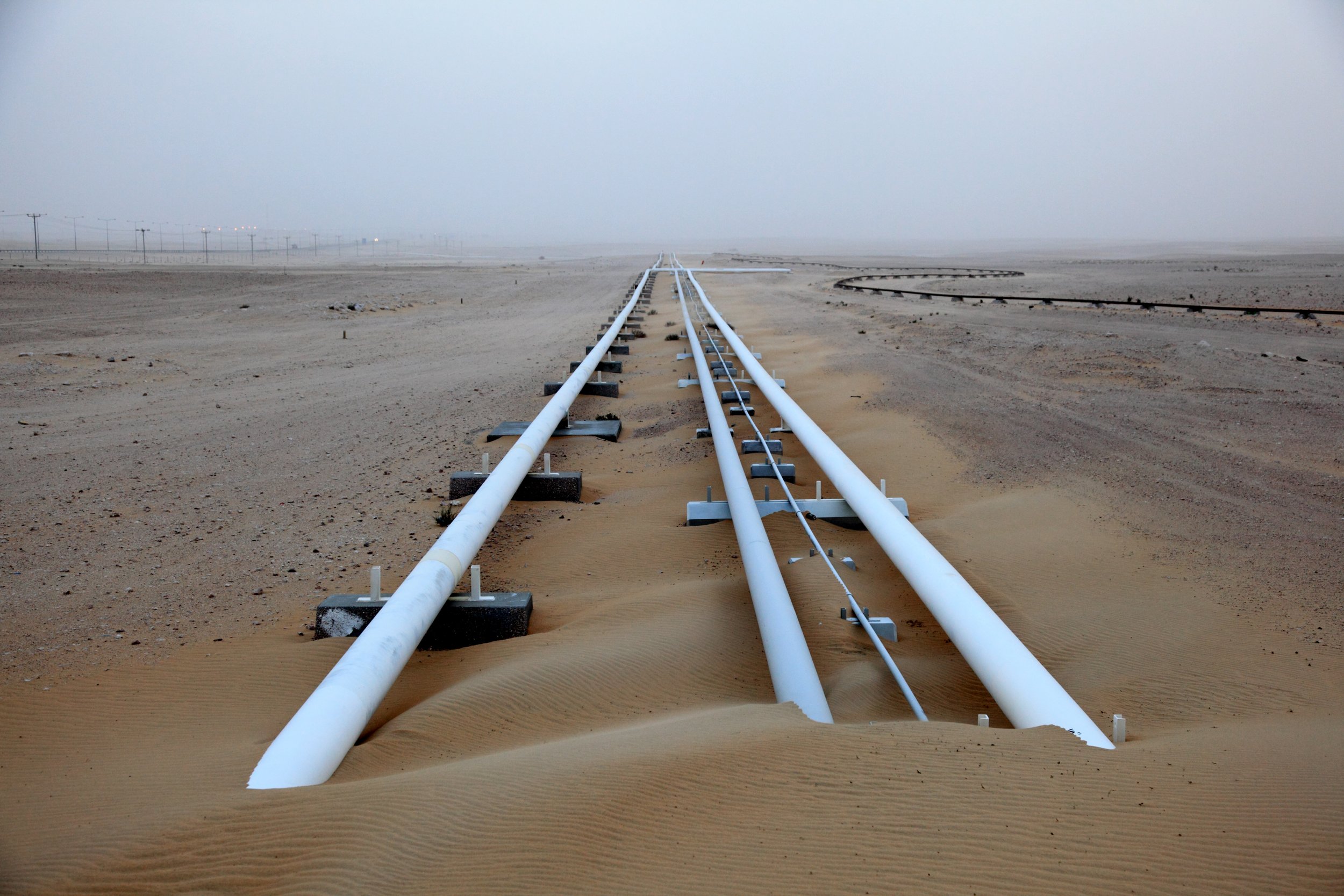 A set of white railroad tracks partially buried in sand, extending into a foggy desert landscape.