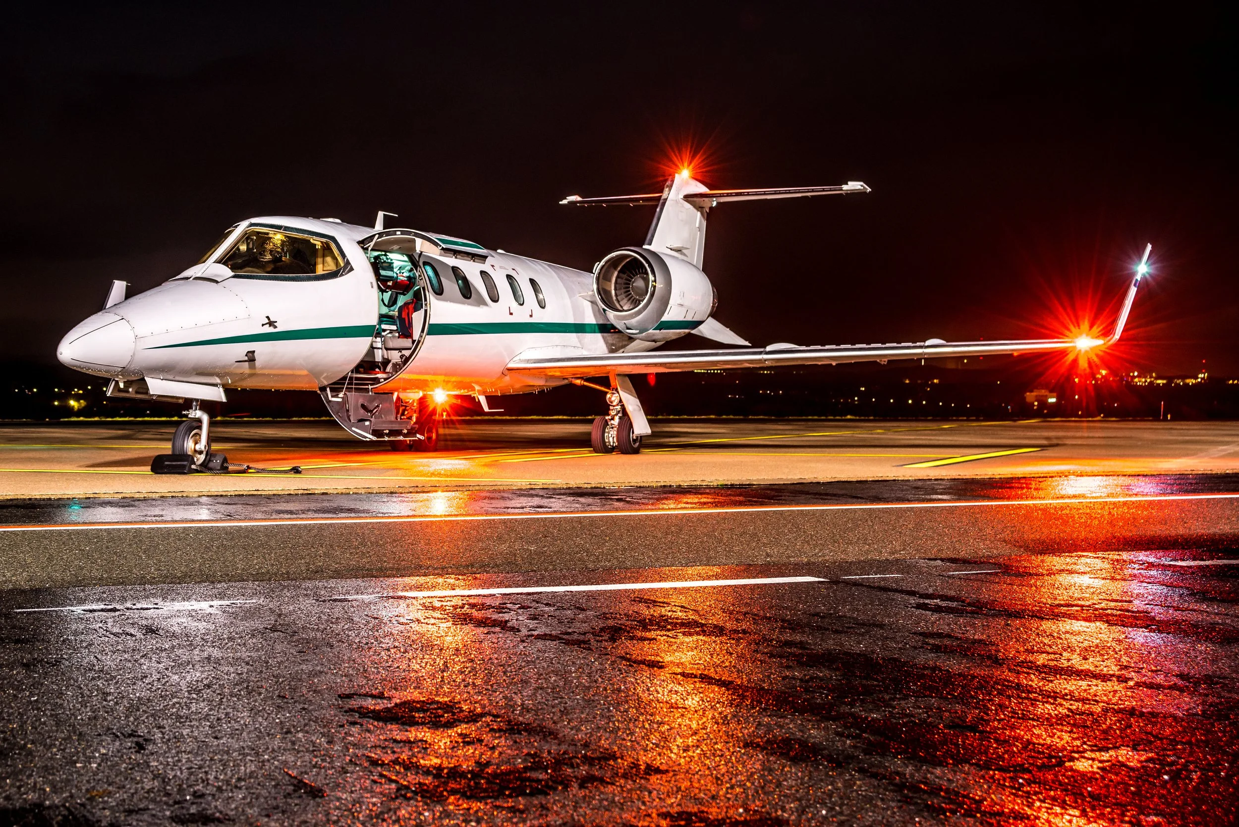 A private jet parked on an airport tarmac at night, illuminated by red and white warning lights.