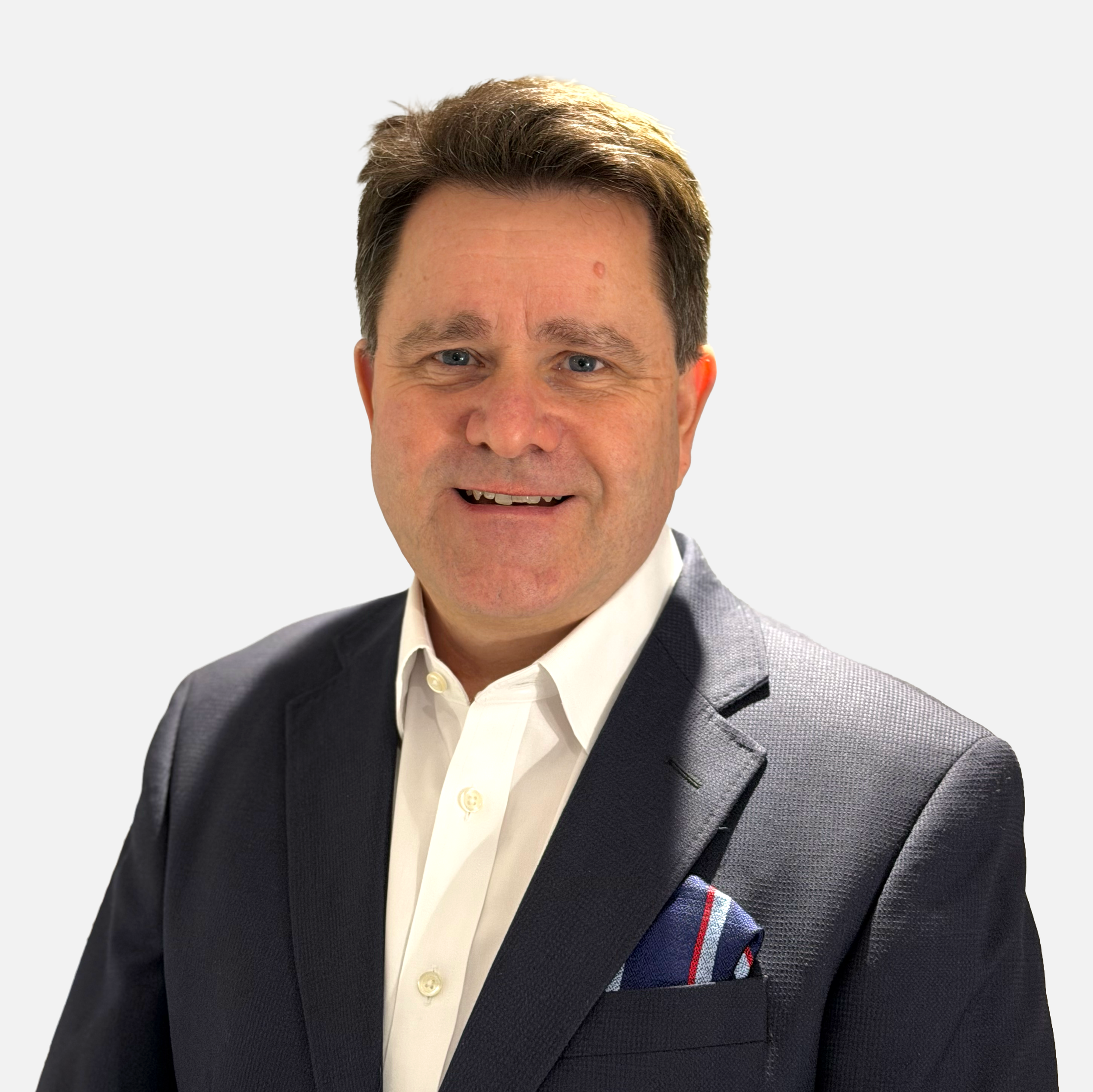 A middle-aged man with brown hair and blue eyes wearing a dark suit jacket, a white dress shirt, and a colorful pocket square, smiling against a plain white background.