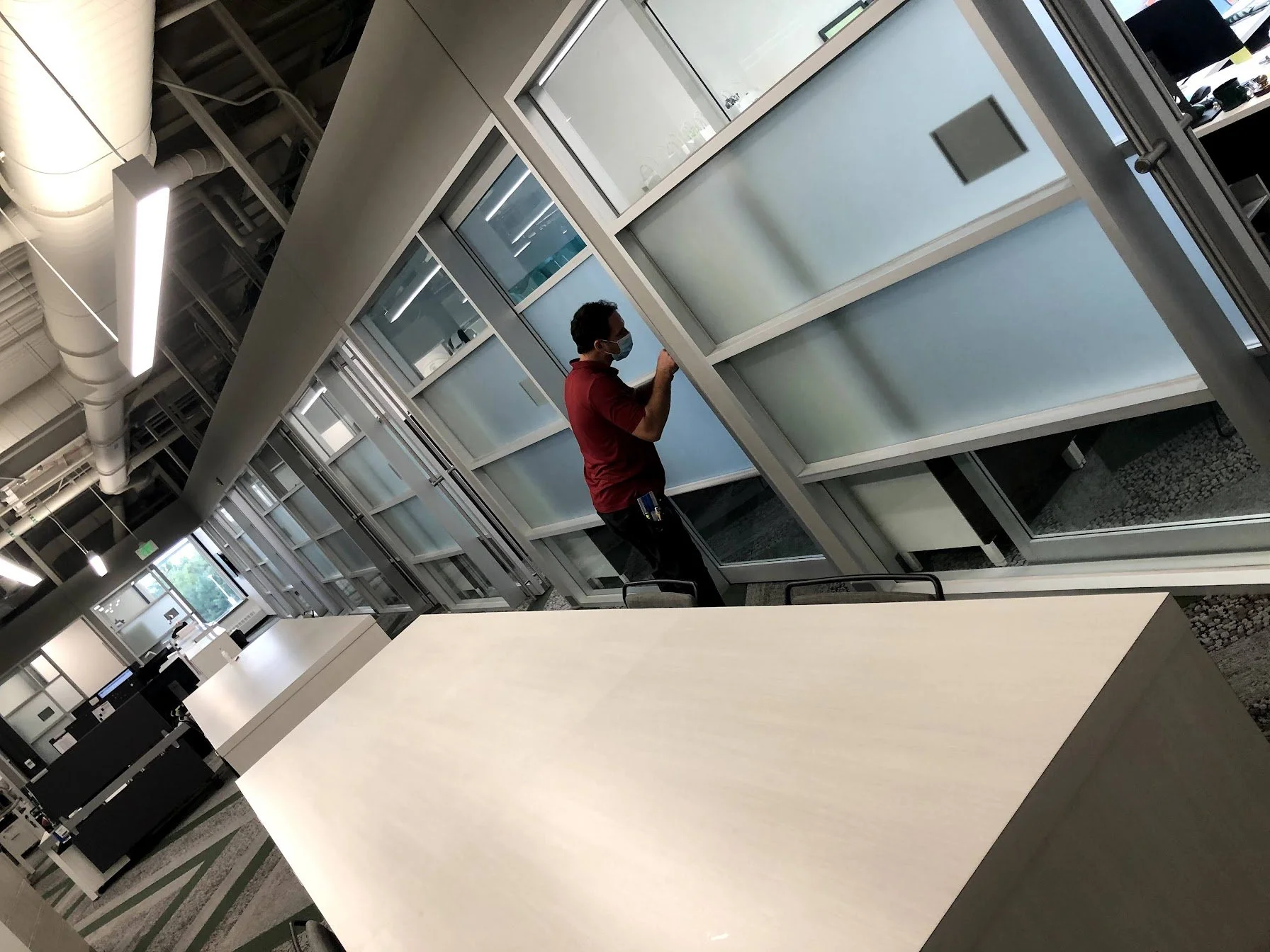 A man wearing a face mask and a red shirt cleaning glass panels in an office renovation area.