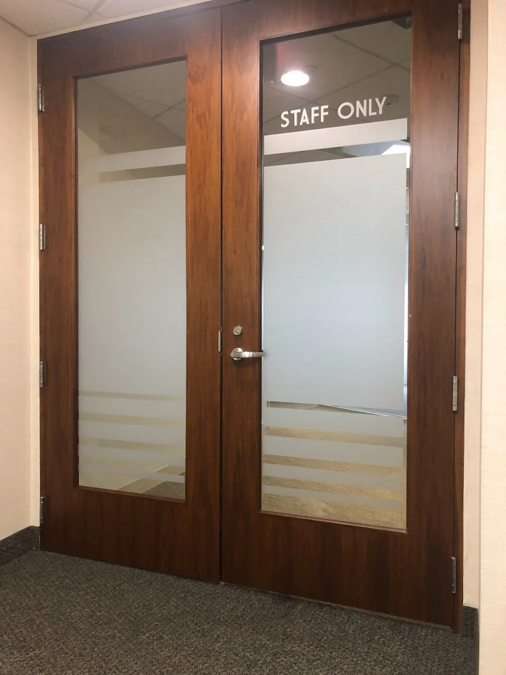 Double wooden door with glass panels, one has a 'STAFF ONLY' sign, leading to a restricted area.