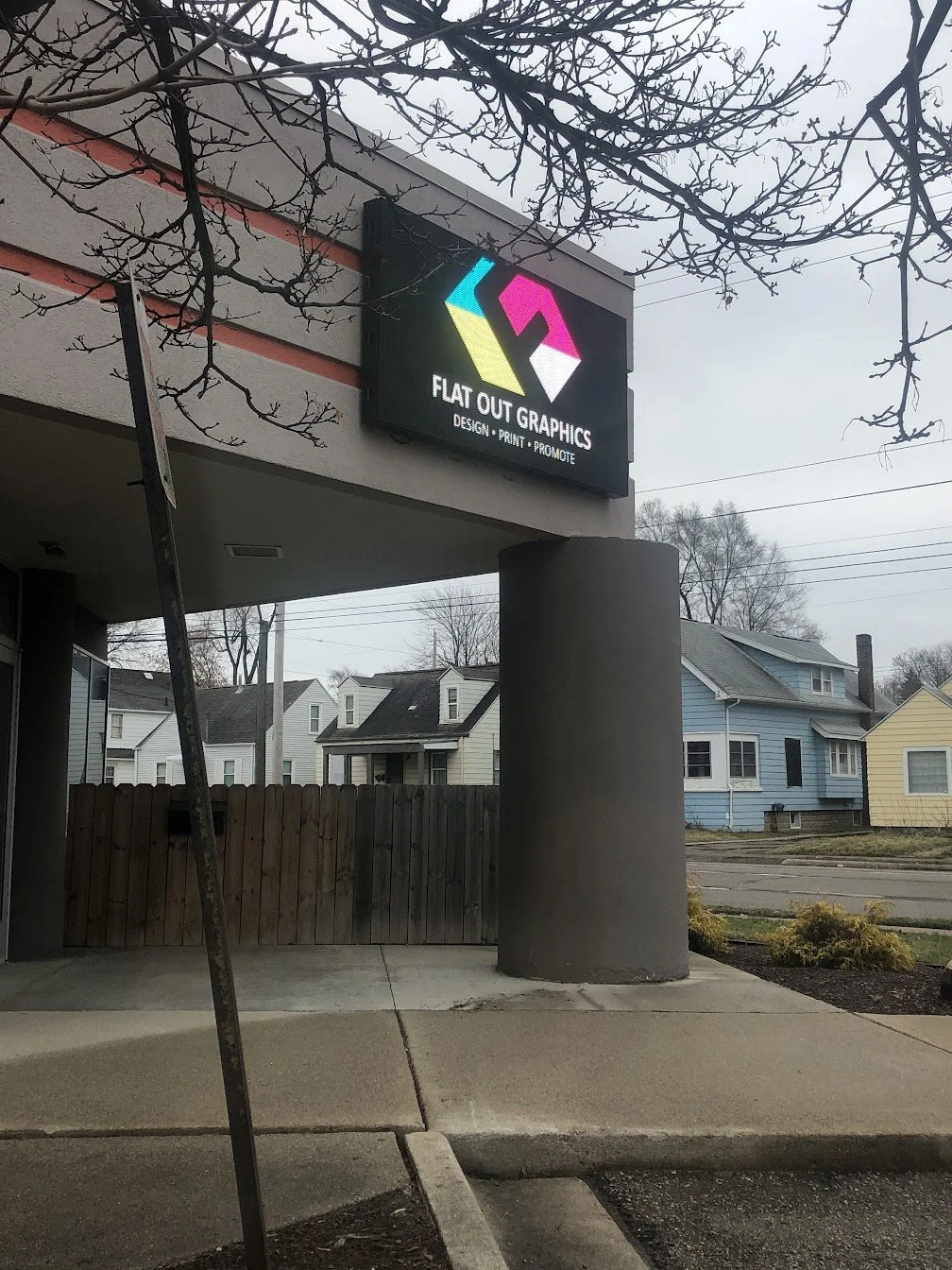 A sign for Flat Out Graphics with a colorful logo and the words 'Design, Print, Promote' on the building's exterior.