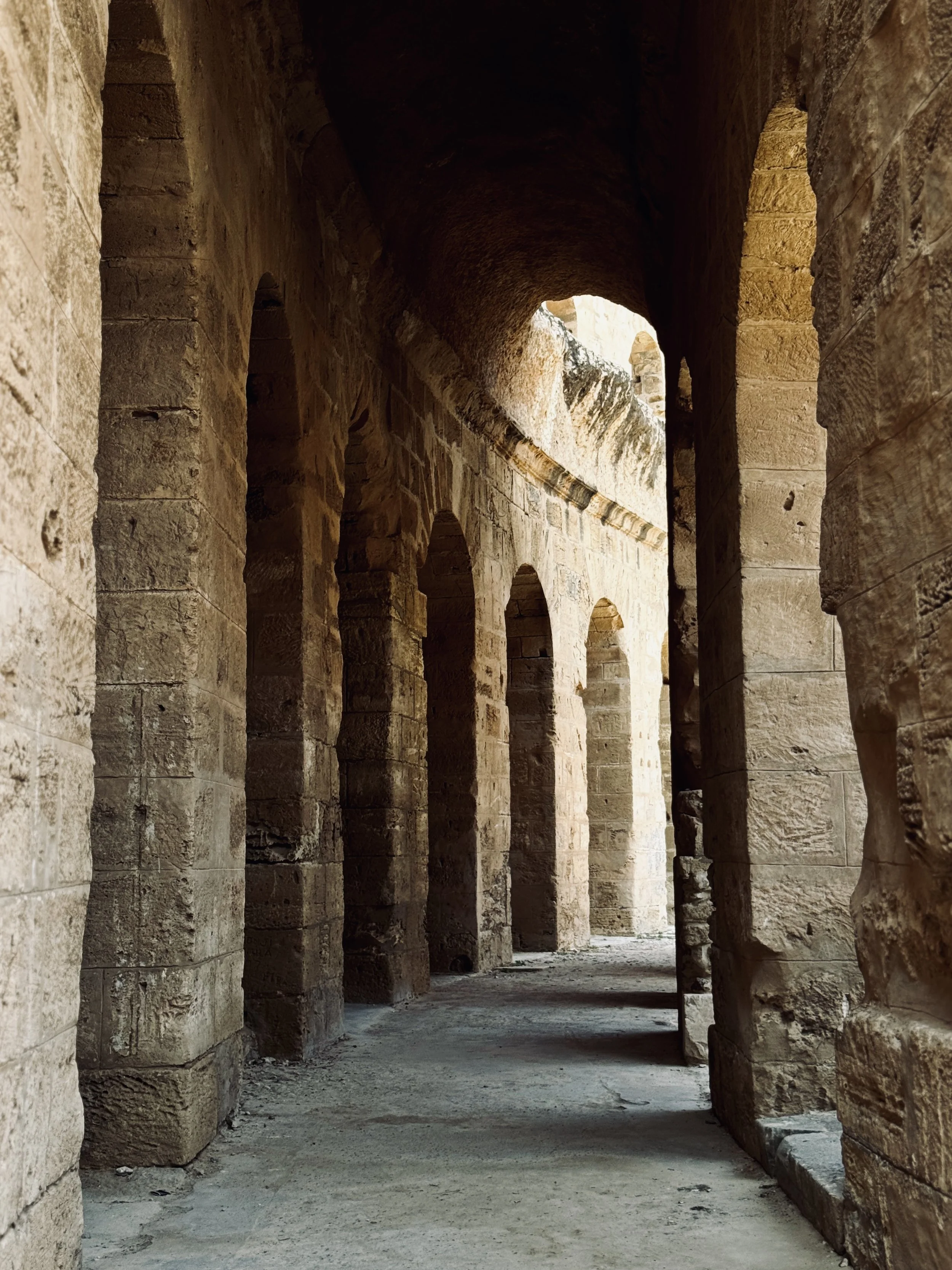 Ancient stone ruins with tall arched doorways and columns, sunlight illuminating parts of the stone walls and ground.