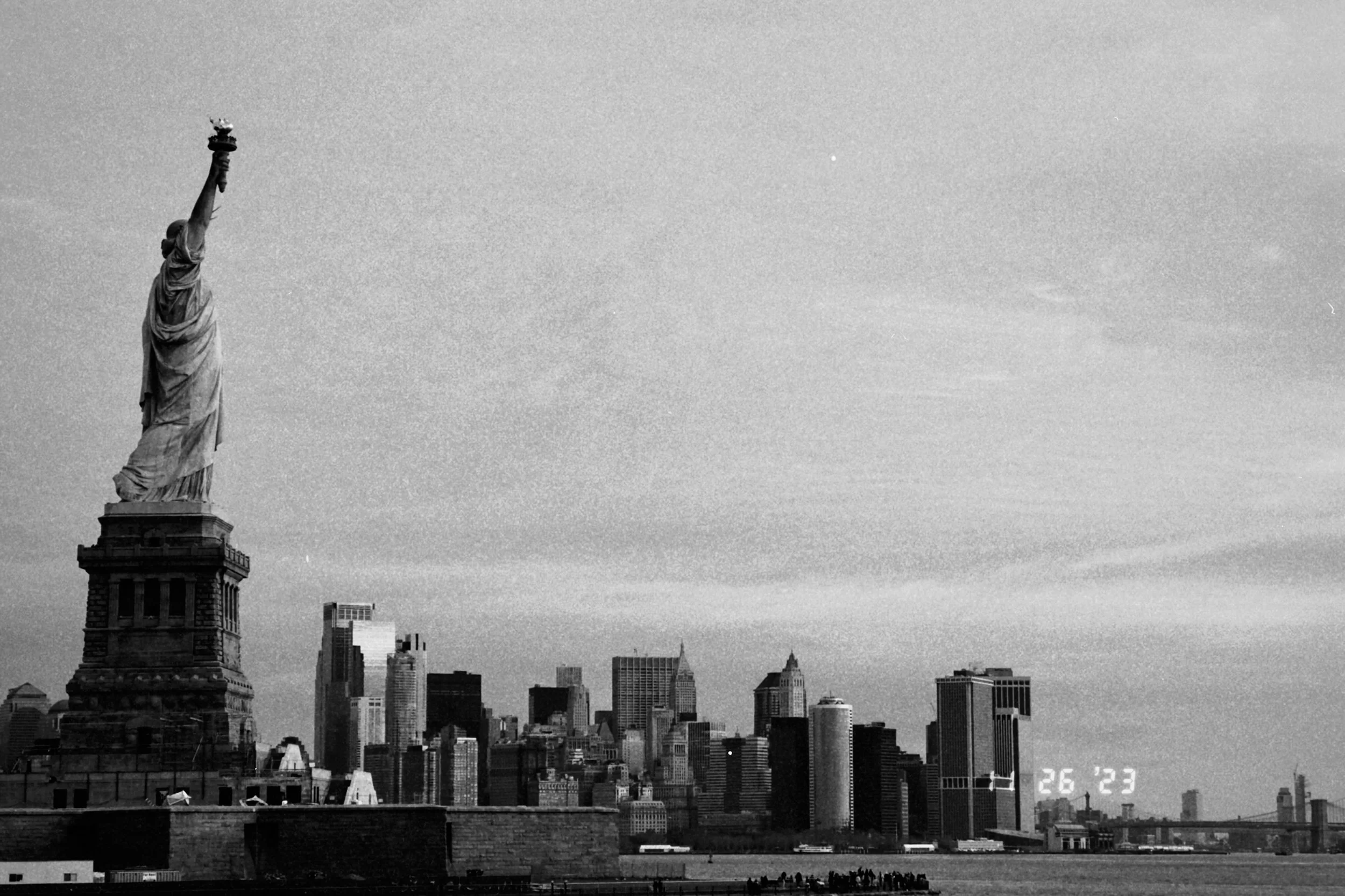 Black and white photo of the New York City skyline, featuring the Statue of Liberty in the foreground and tall skyscrapers in the background.