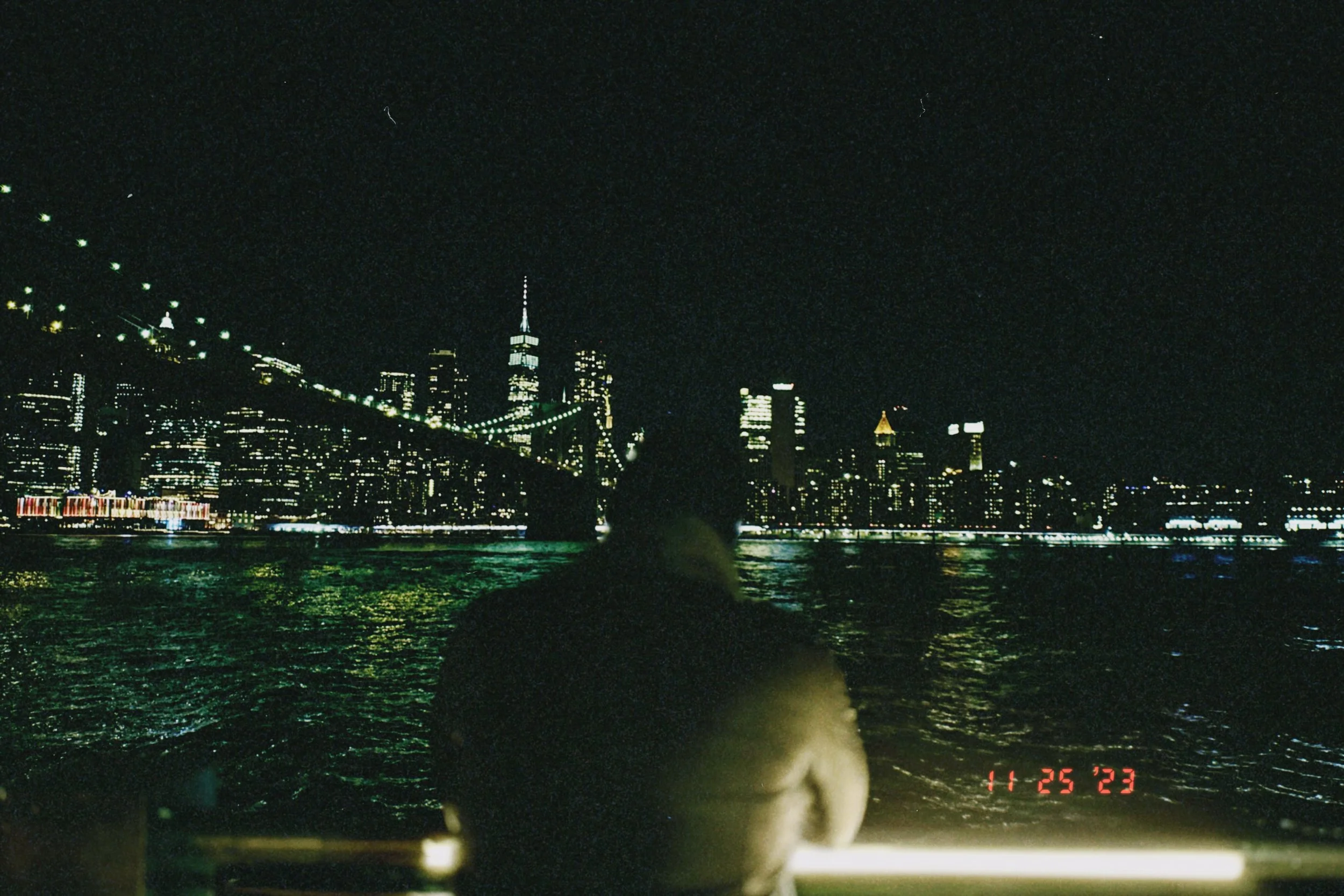 Nighttime view of the New York City skyline with the Brooklyn Bridge in the foreground and the One World Trade Center illuminated in the distance.