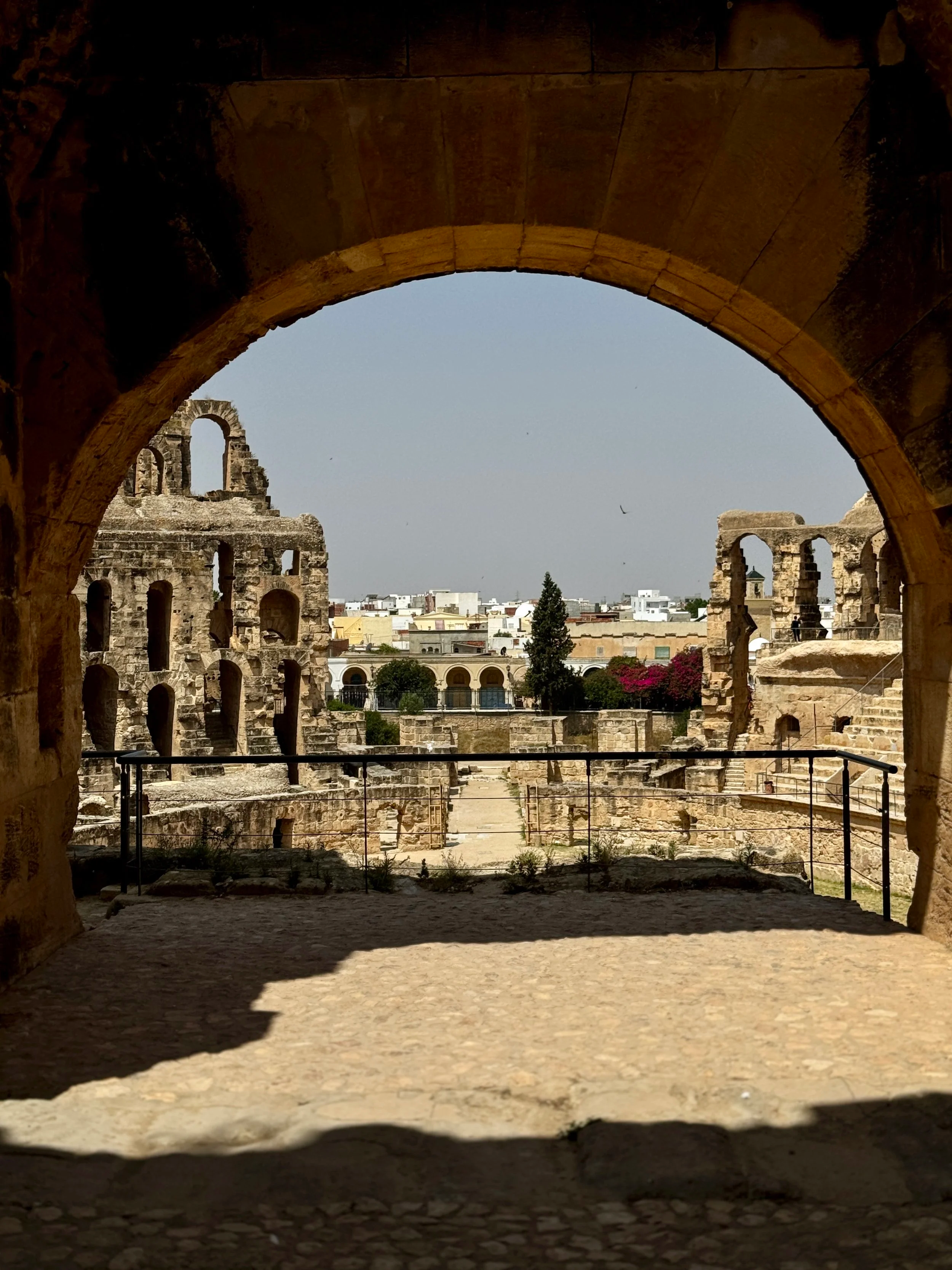 Ancient stone ruins seen through a dark arched opening, with a cityscape and trees in the background.