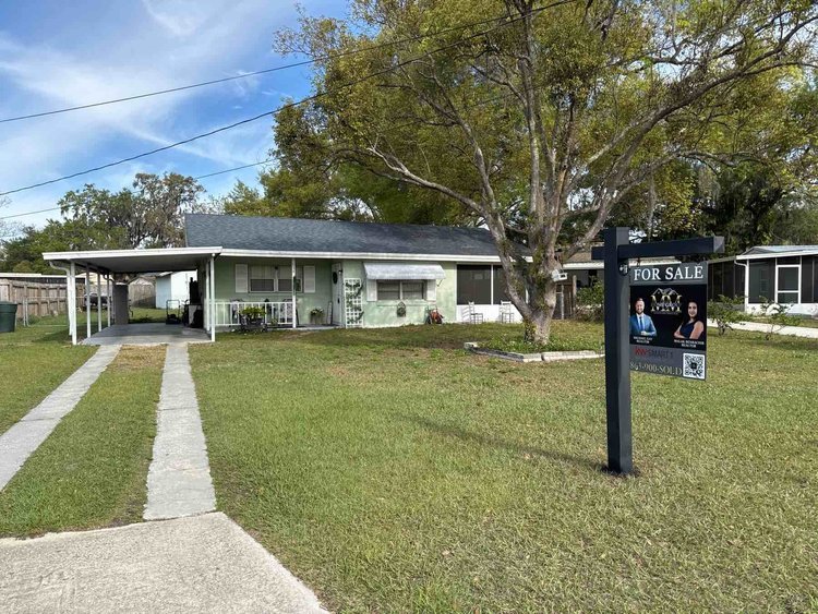 Front yard of a house with a lawn, driveway, and a large tree. There is a sign post