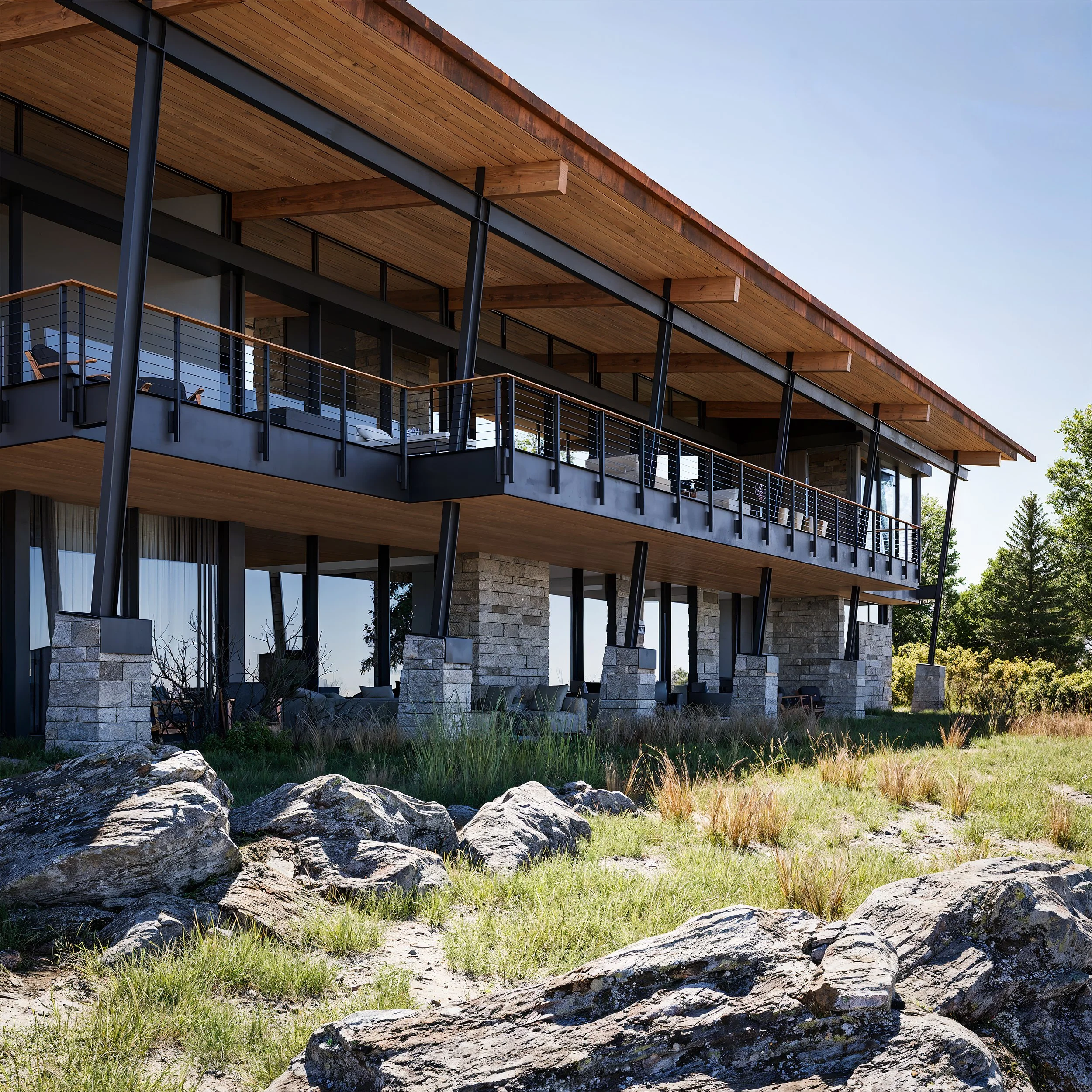 A modern two-story house with large glass windows, a spacious balcony with black railing, supported by black steel beams, and made of stone, wood, and metal, surrounded by rocks and grassy area, with trees in the background under a clear blue sky.