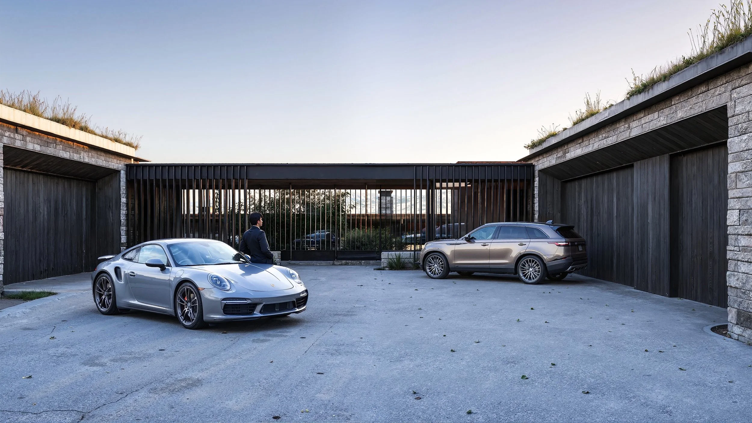Luxury garage with two parked cars and a man in a suit standing next to a silver sports car.