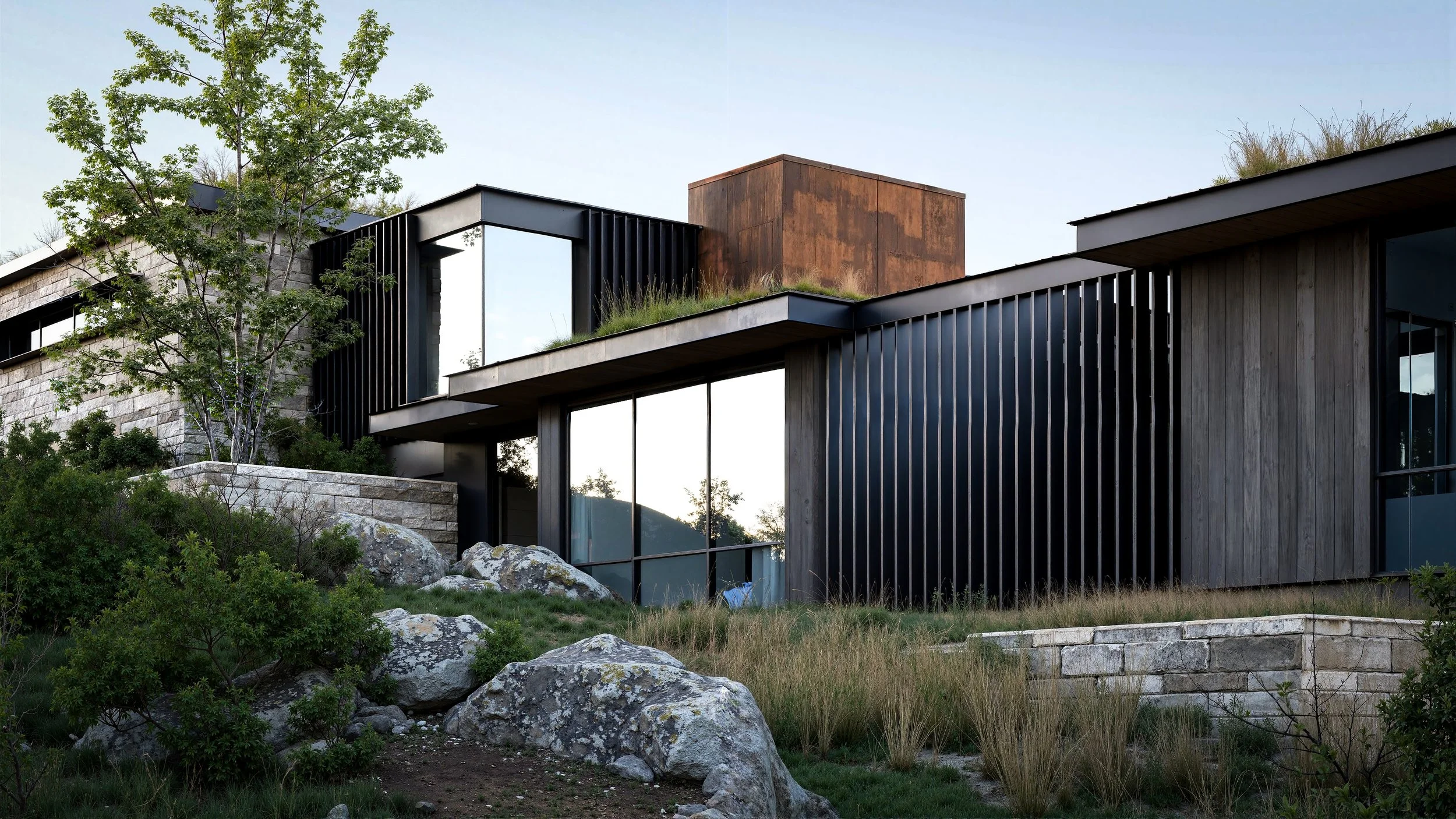 Modern house with large glass windows, black vertical slats, and a rooftop garden, surrounded by rocks and greenery.